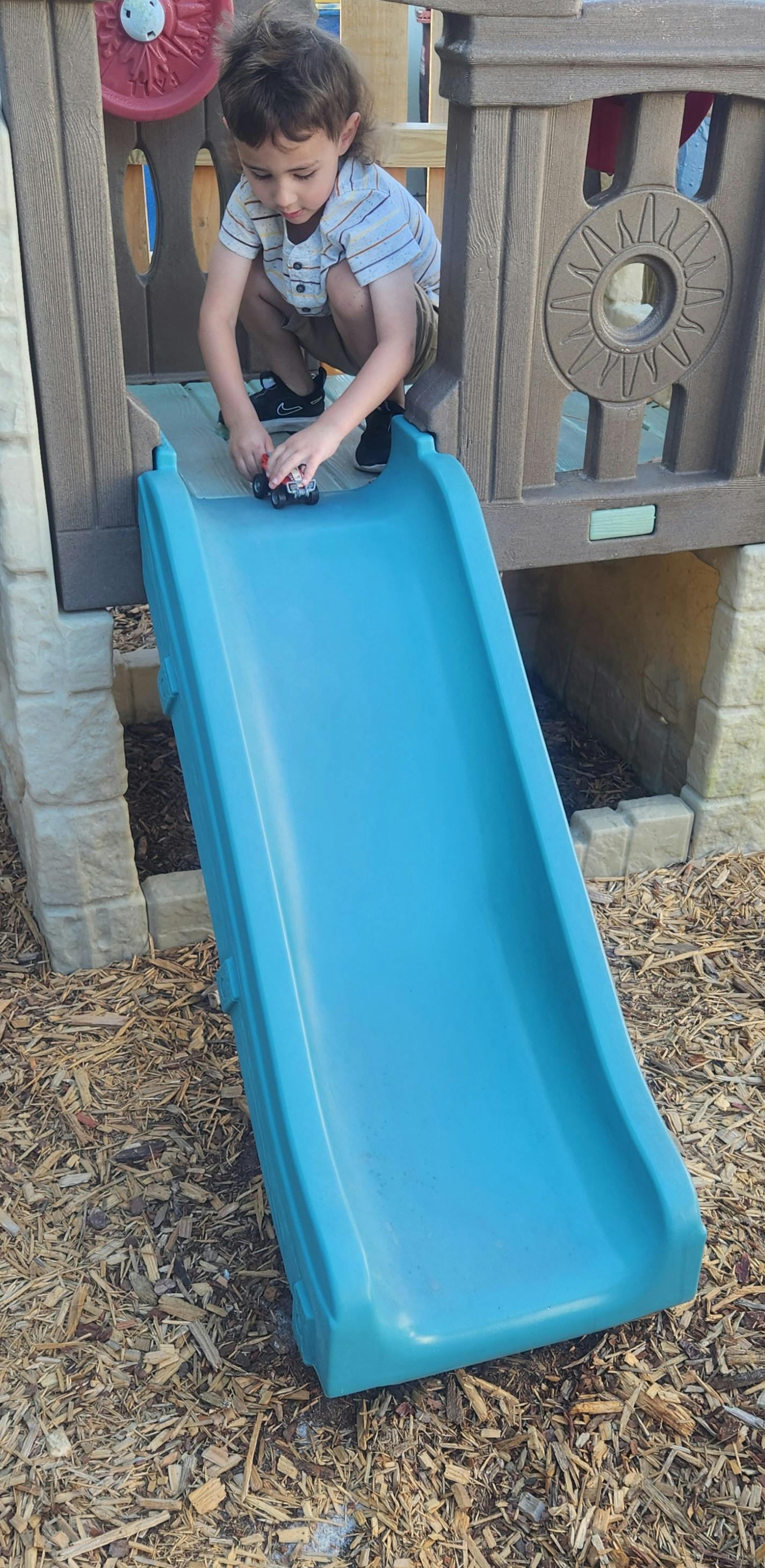 Child playing with a toy car on a blue slide