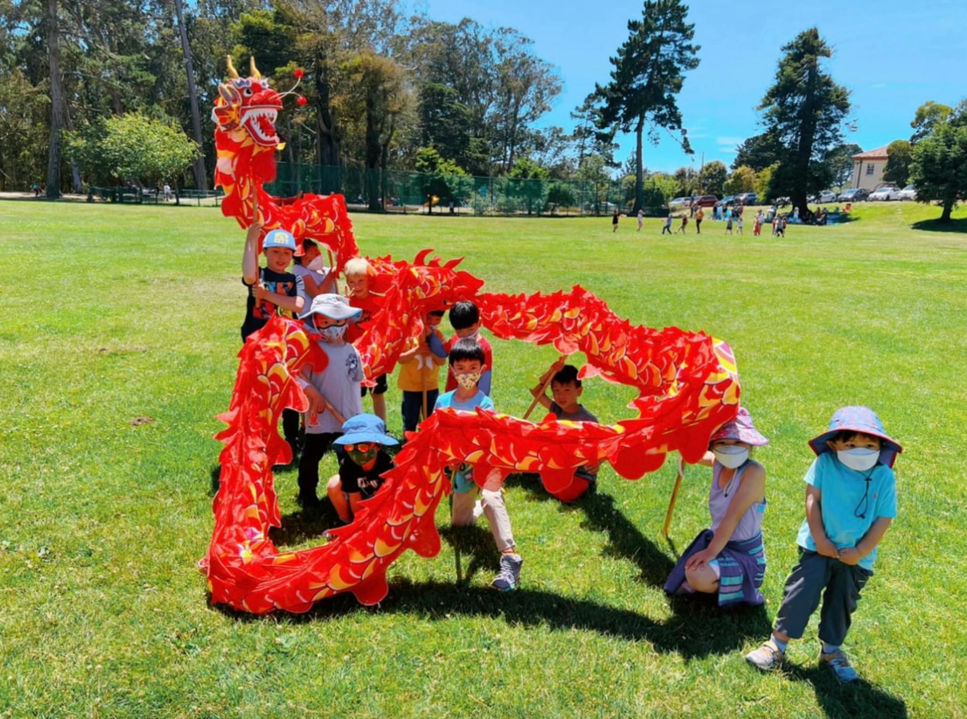 Children holding a red dragon costume on a grassy field