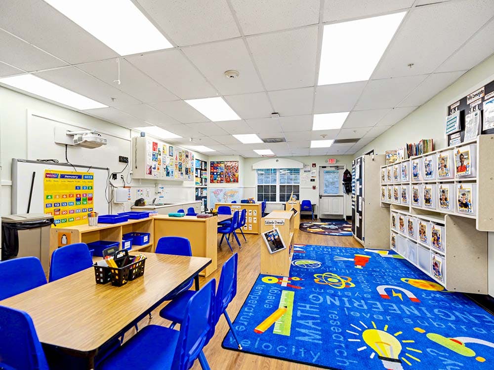 Classroom with blue chairs, tables, and a blue rug with educational words