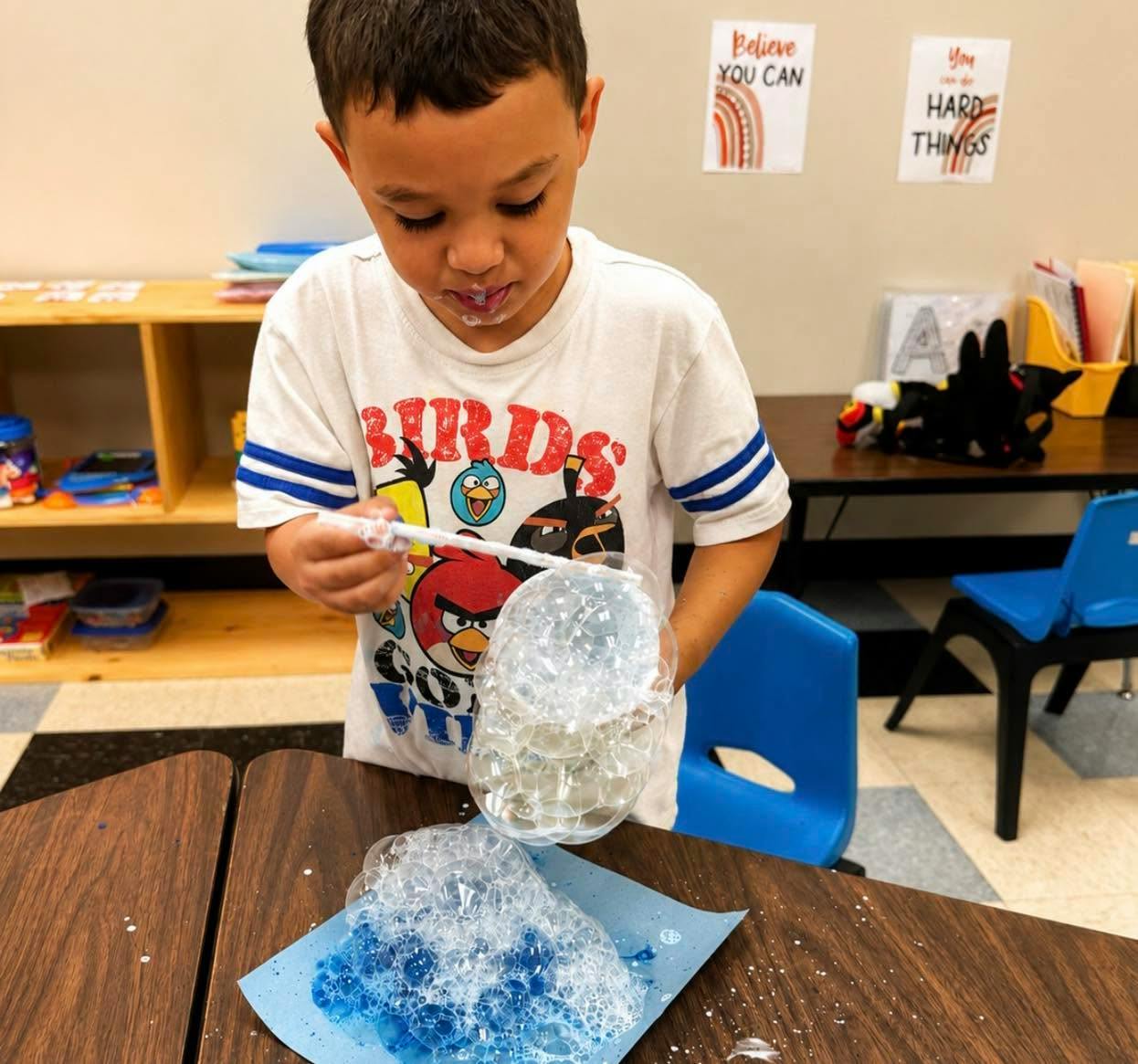 Child blowing bubbles onto paper at a desk
