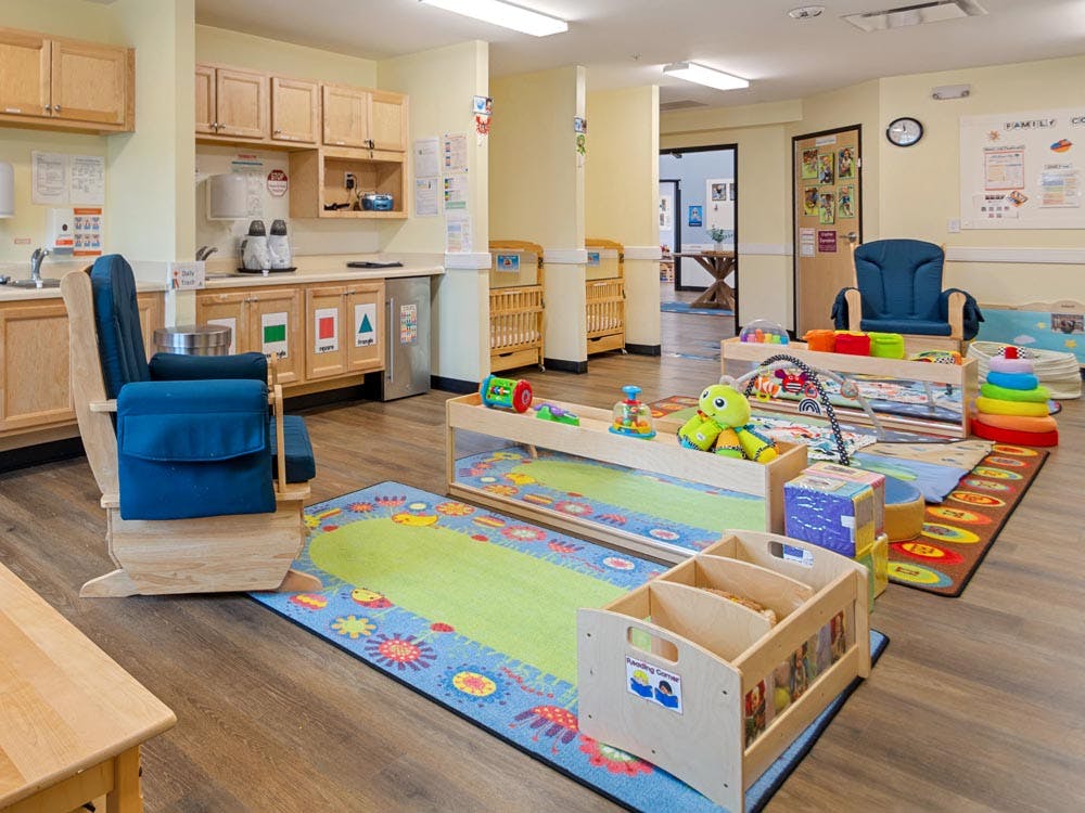Baby classroom with activity mats, toys, cribs, and a changing station