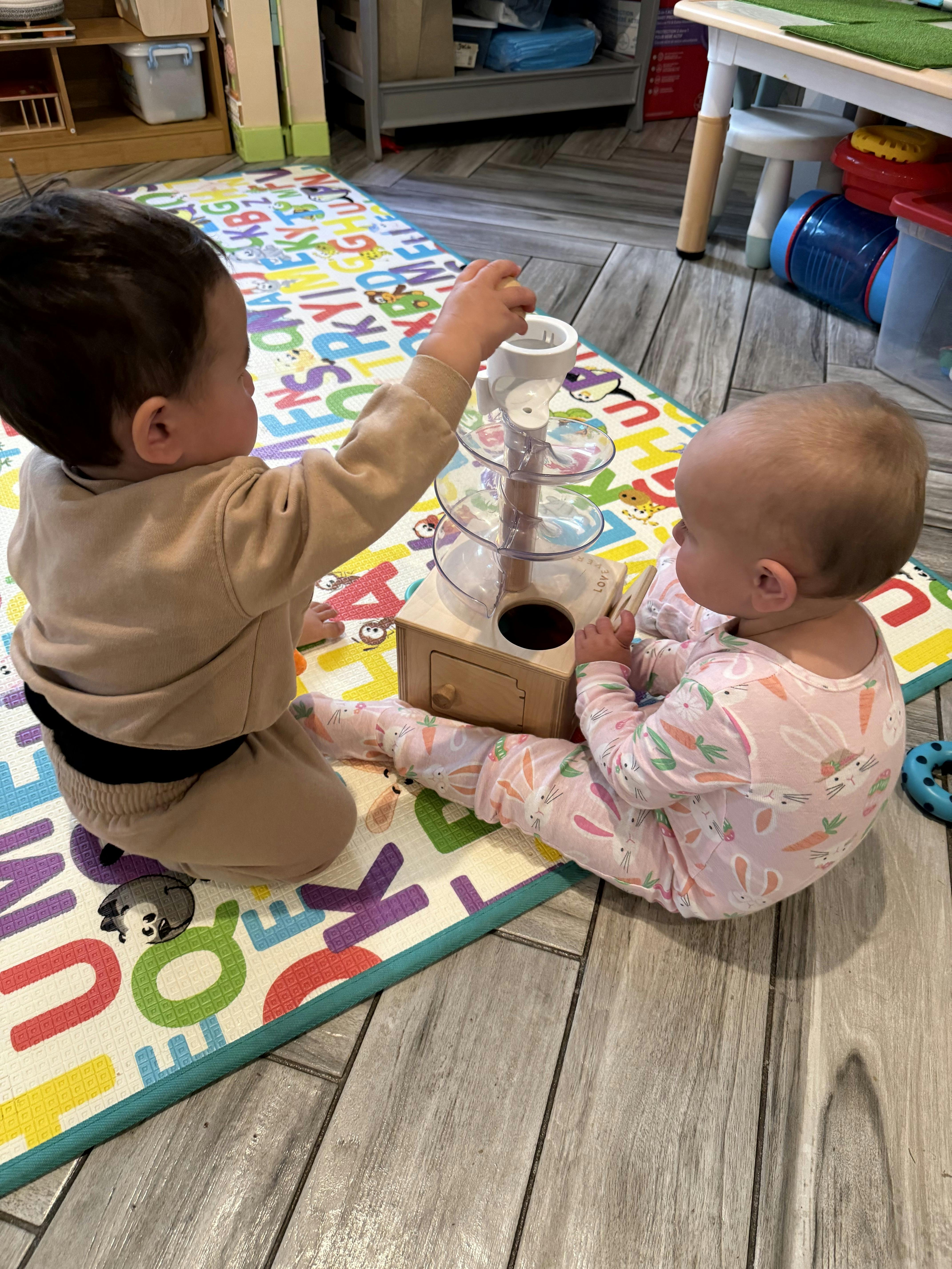 Two children playing with a wooden and clear plastic ball run toy