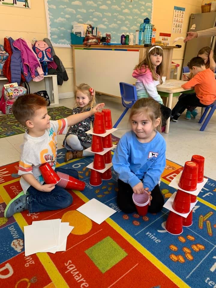 Children building towers with red cups in a classroom