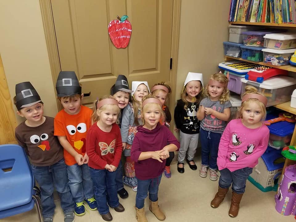 Group of children in a classroom, some wearing hats