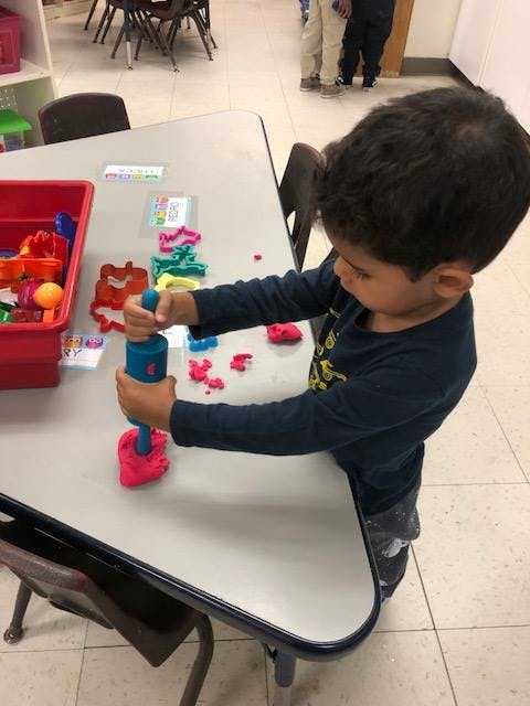 Child playing with play-doh and a play-doh press on a table