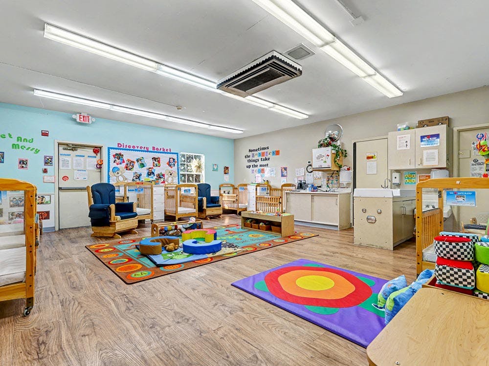 daycare classroom with multiple cribs, rockers, changing station, and play mats
