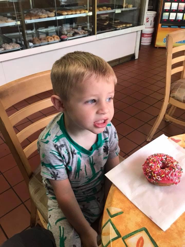 Child sitting at a table with a donut on a paper