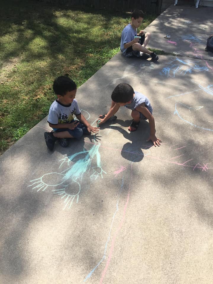 Three children drawing with chalk on a sidewalk