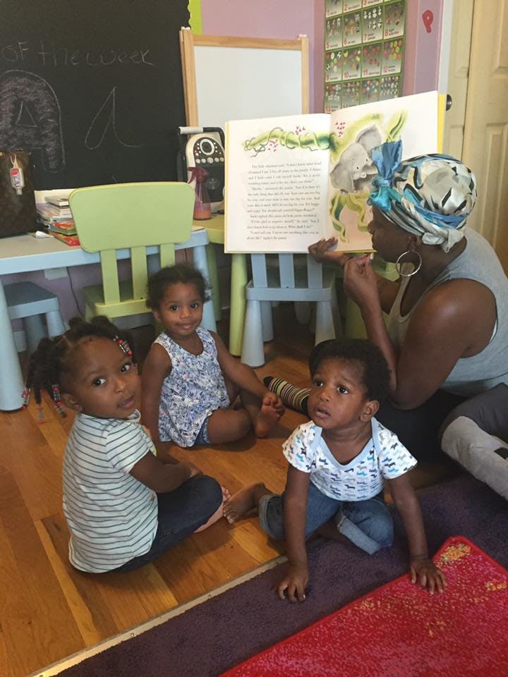 Person reading a book to three children sitting on the floor
