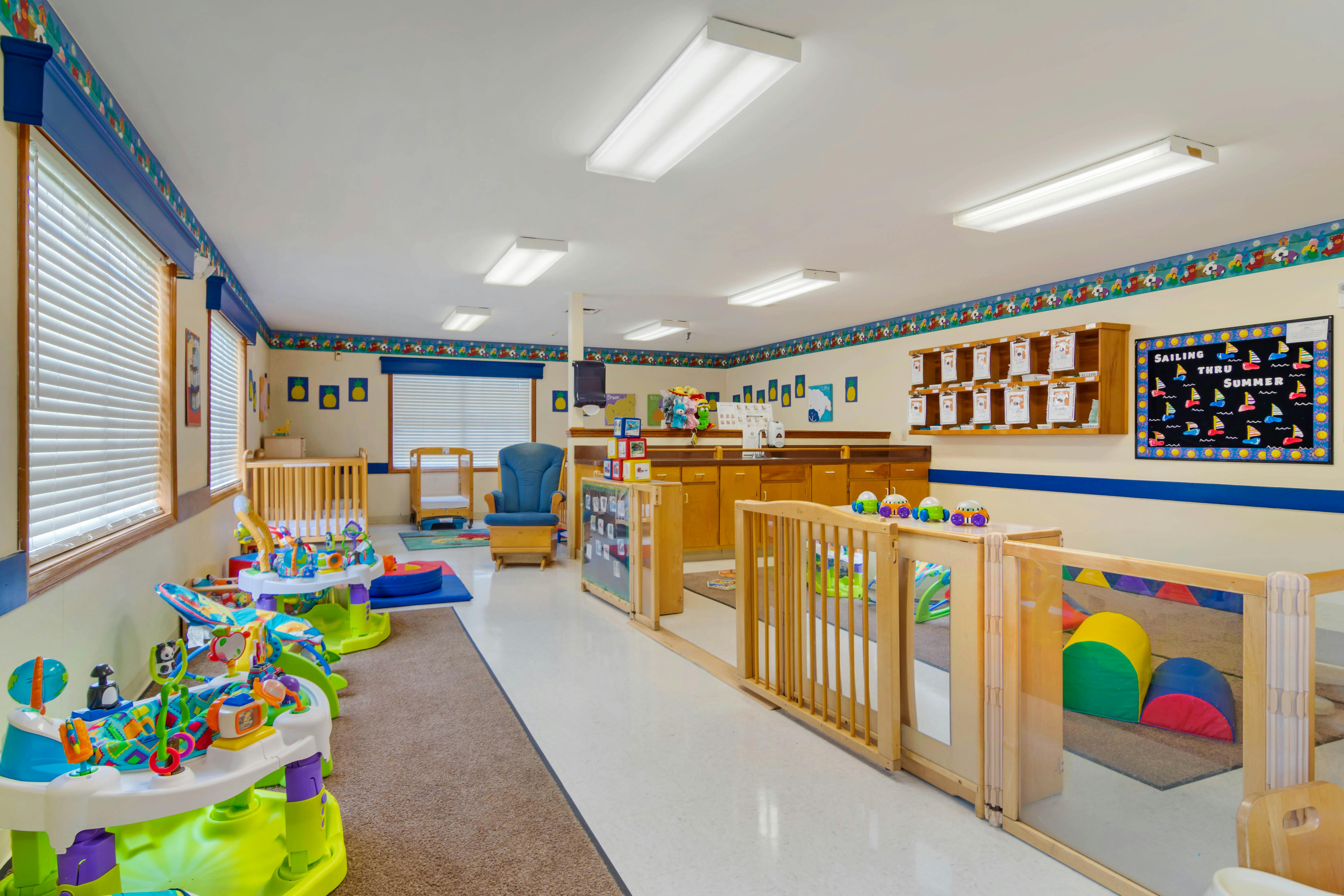 A childcare room with cribs, play mats, and developmental toys