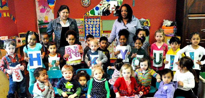 Two people with a group of children holding up letters in a classroom