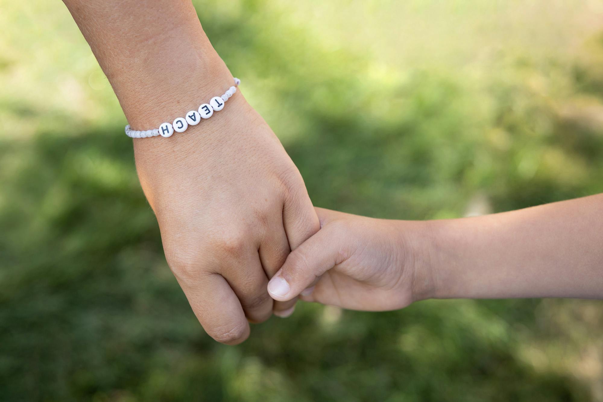 Person wearing a bracelet that says TEACH holding hands with a child