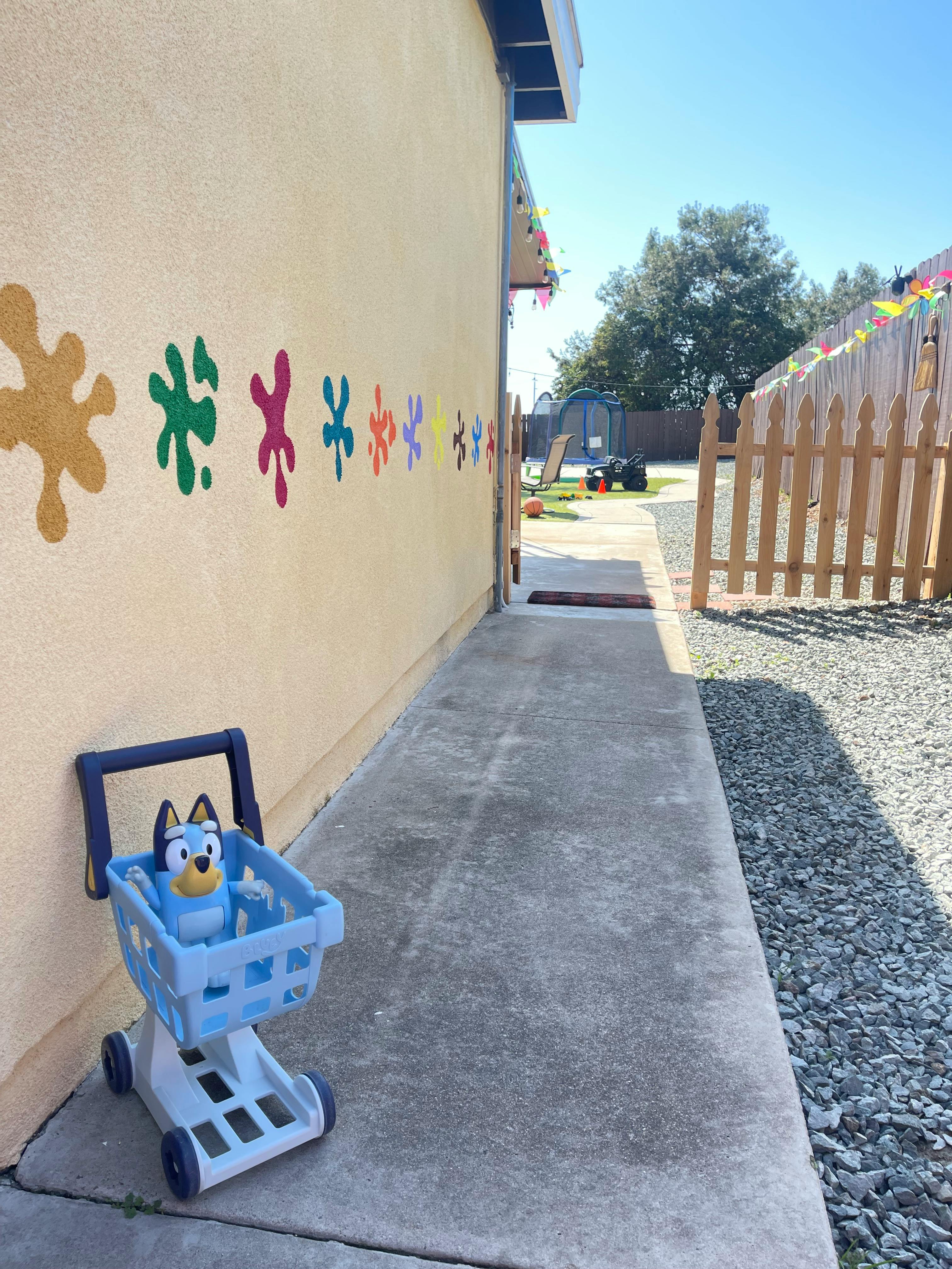 Toy shopping cart with a blue dog toy inside next to a wall with paint splatters
