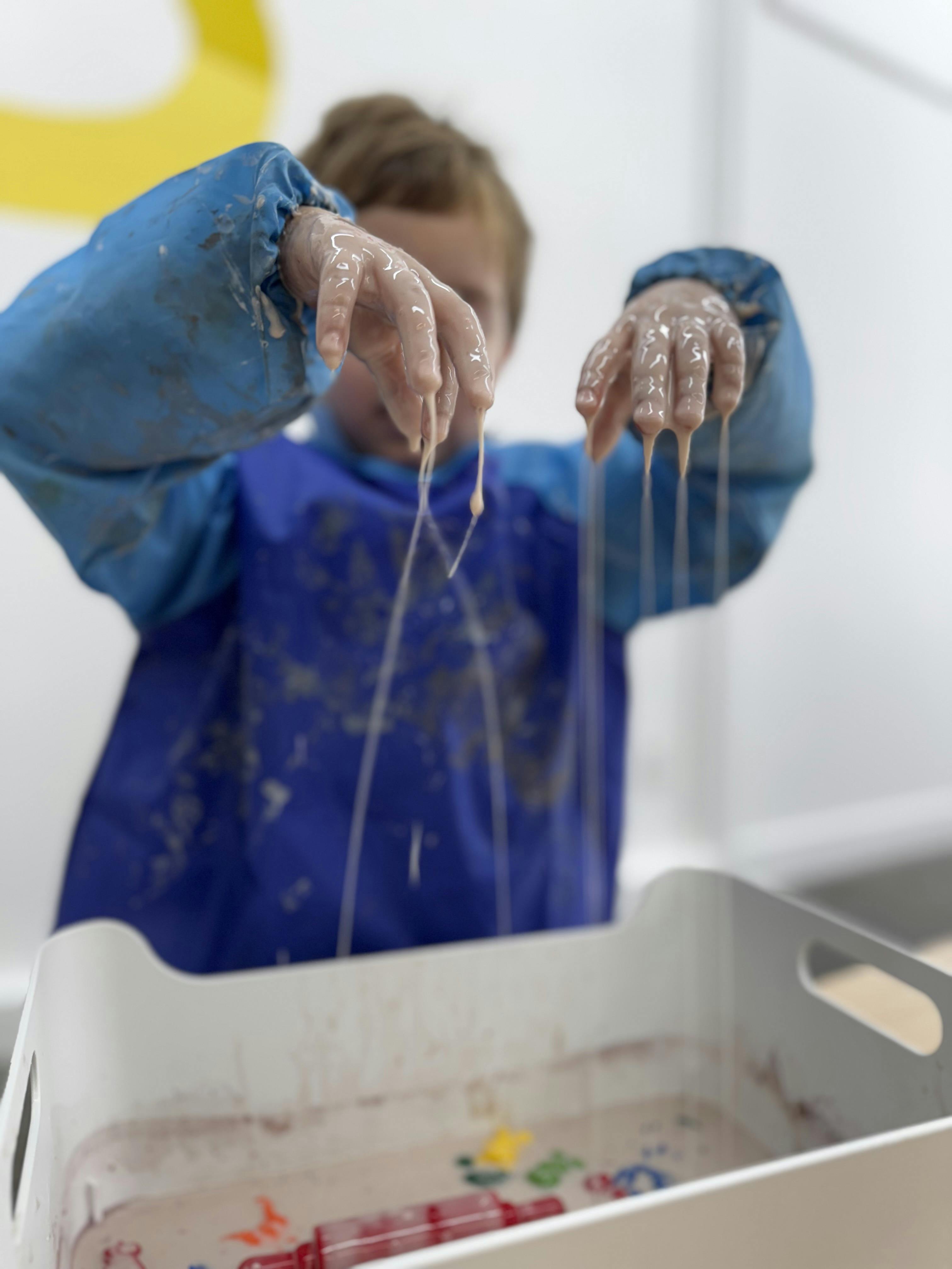 Child in a blue smock playing with slime in a tray