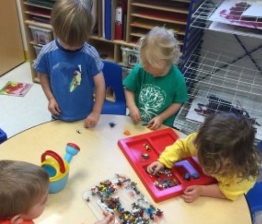 Children playing with small toys at a table in a classroom