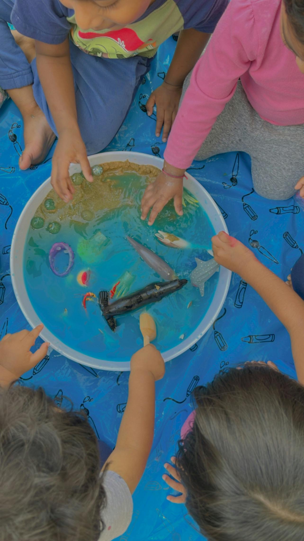 Children playing with toy sea animals and sand in a bowl of water