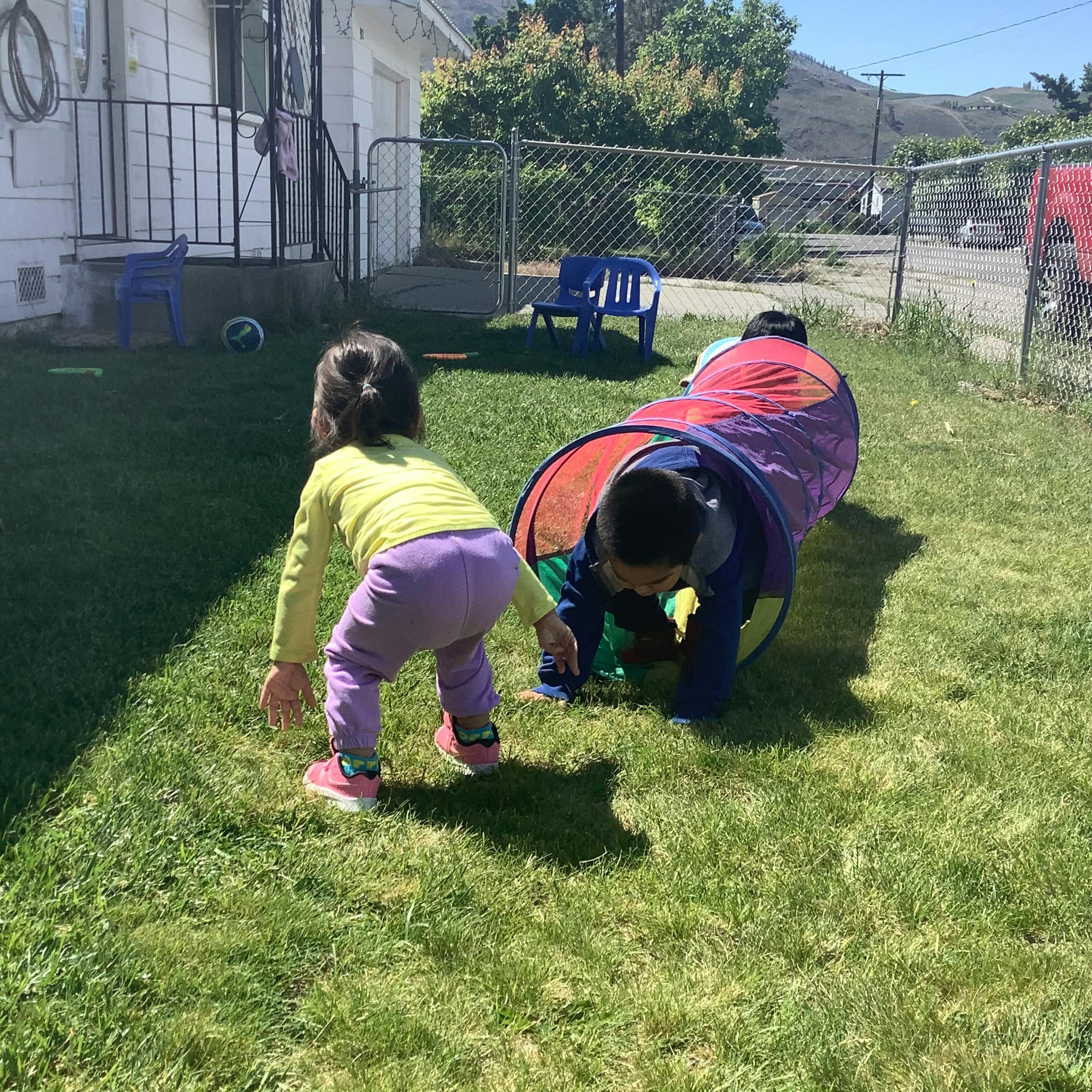 Child crawling through a play tunnel, another child nearby