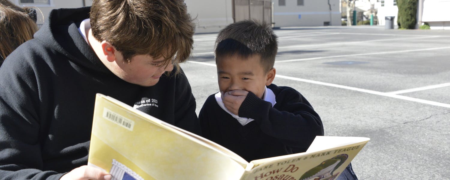 A teen and child read a book together outdoors