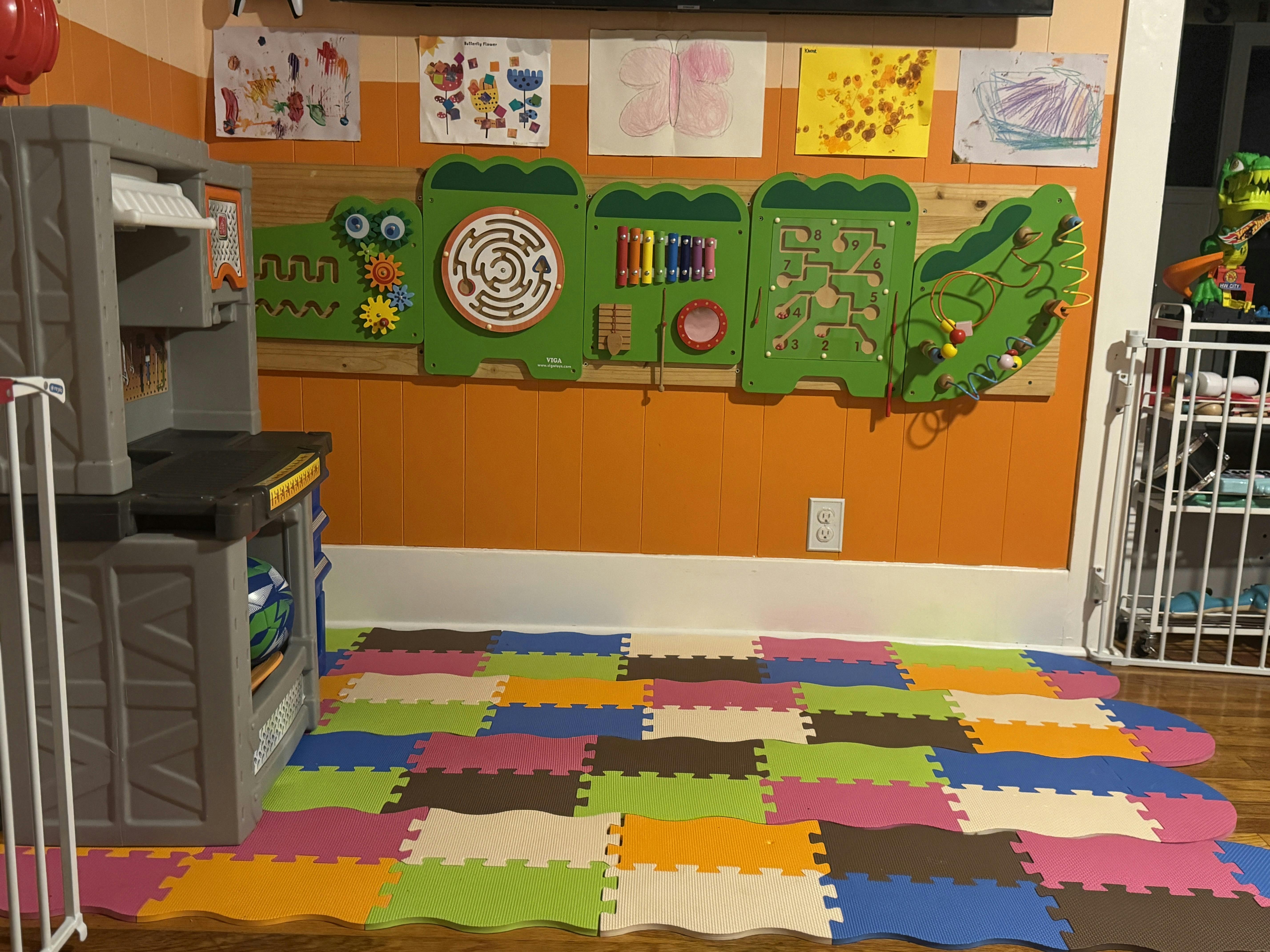 Children's play area with a workbench, wall-mounted activity boards, and foam floor tiles