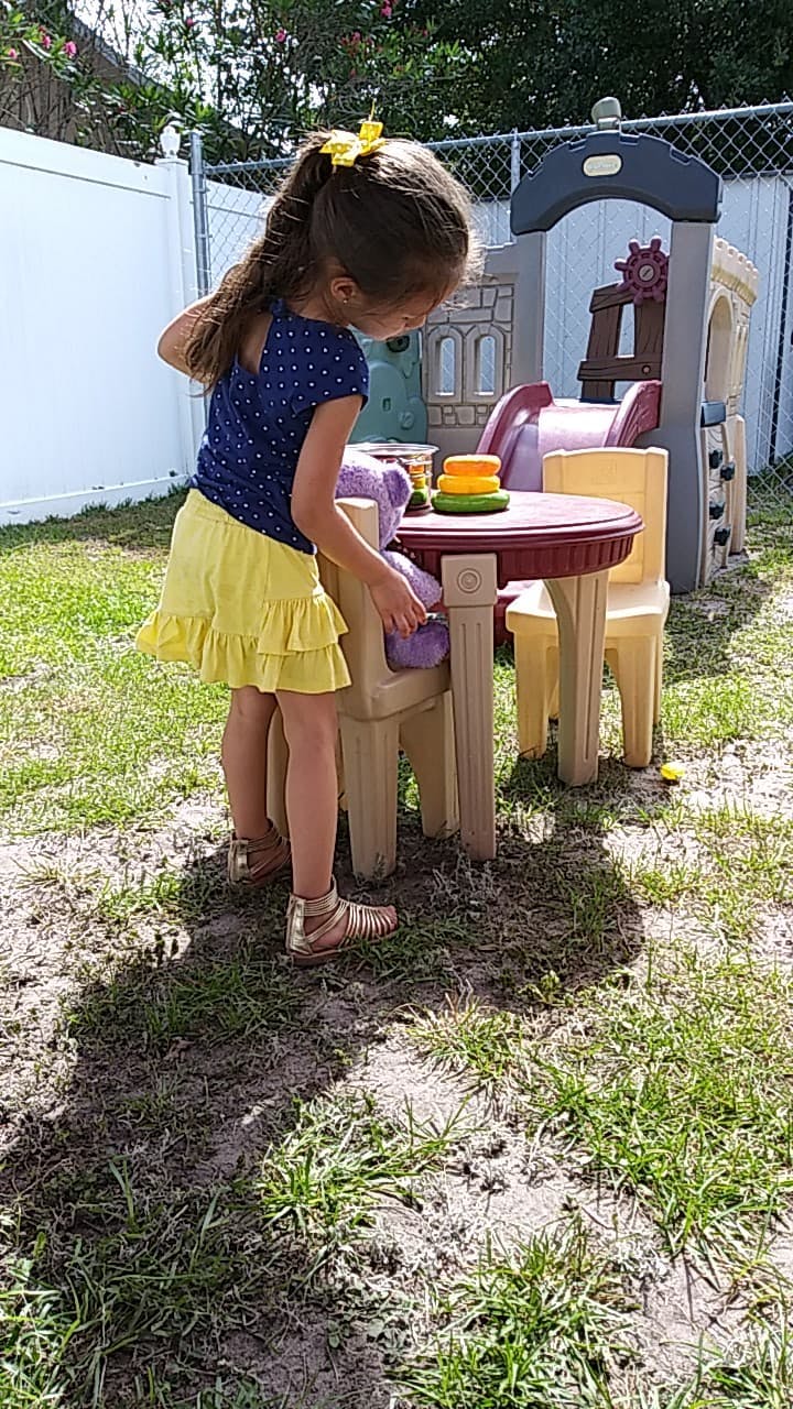Child standing next to a small table and chairs outdoors