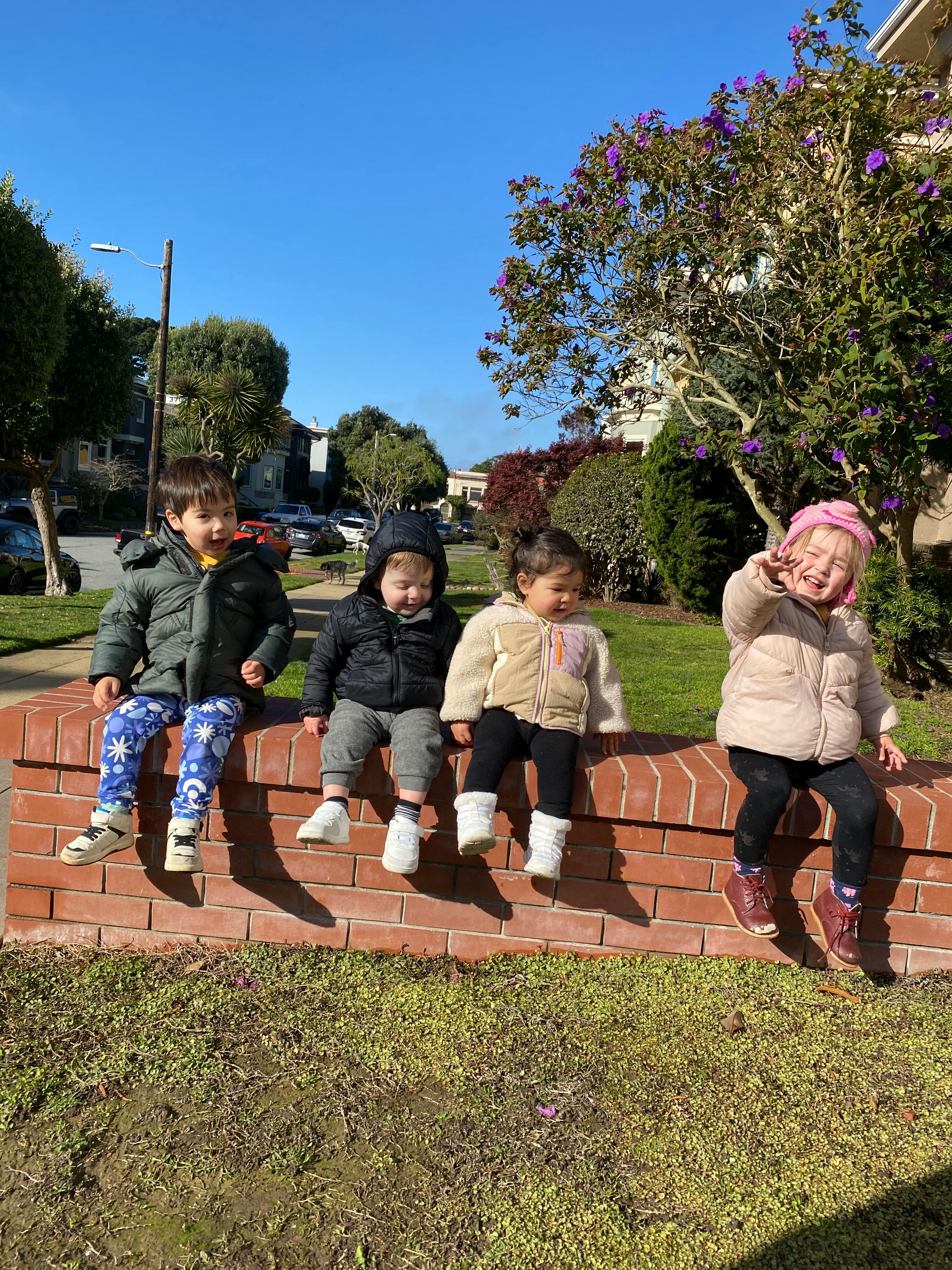 Four children sitting on a brick wall outdoors