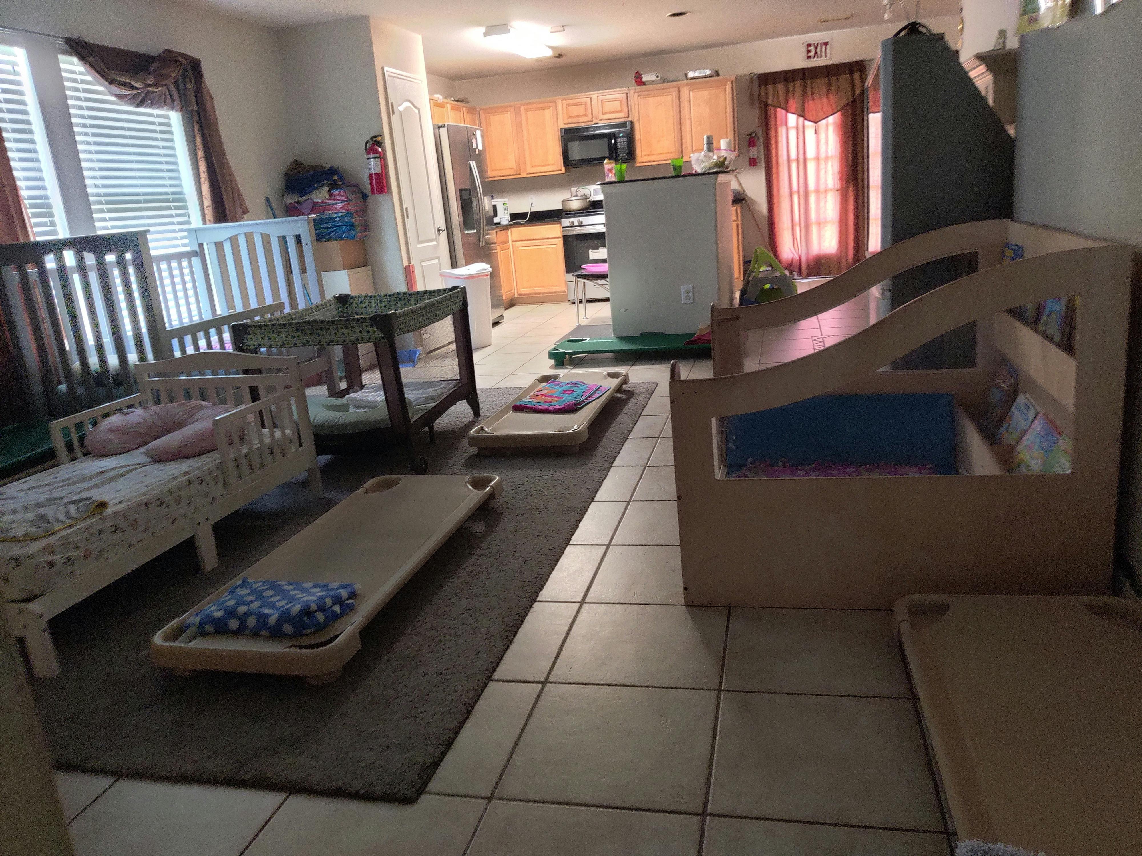 Daycare room with cribs and cots, kitchen in background