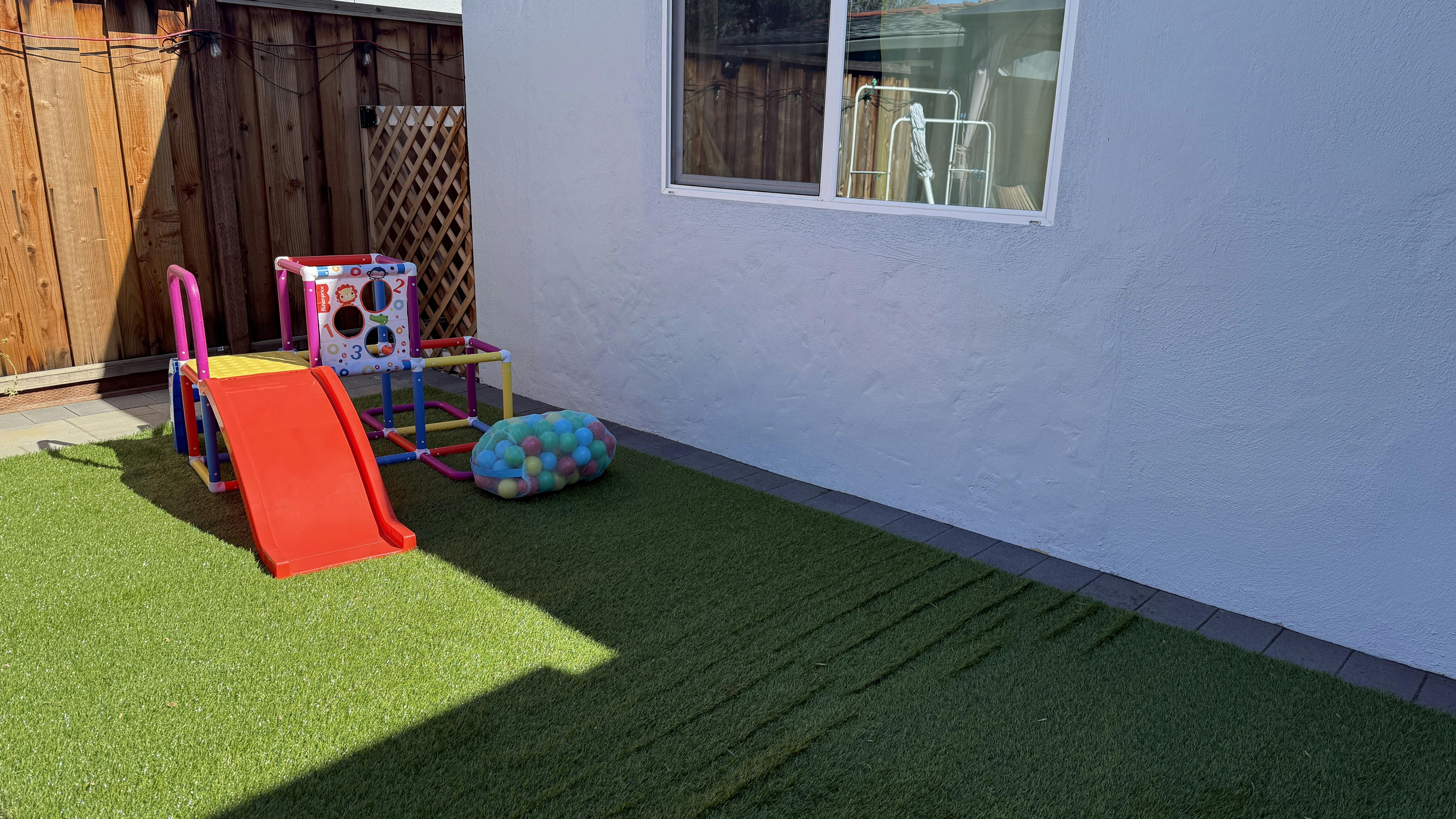Children's playset with a red slide and a bag of colorful balls on artificial grass