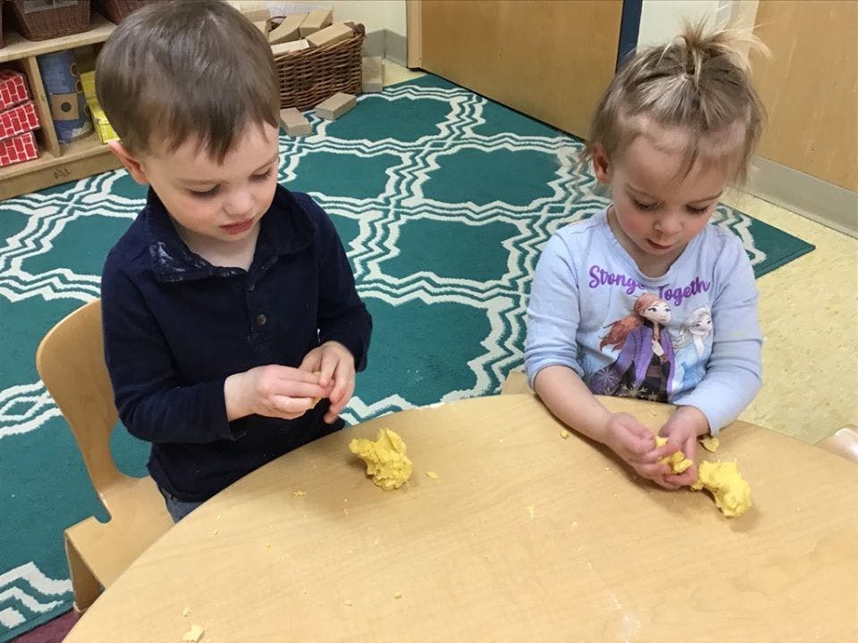 Two children playing with yellow dough at a table