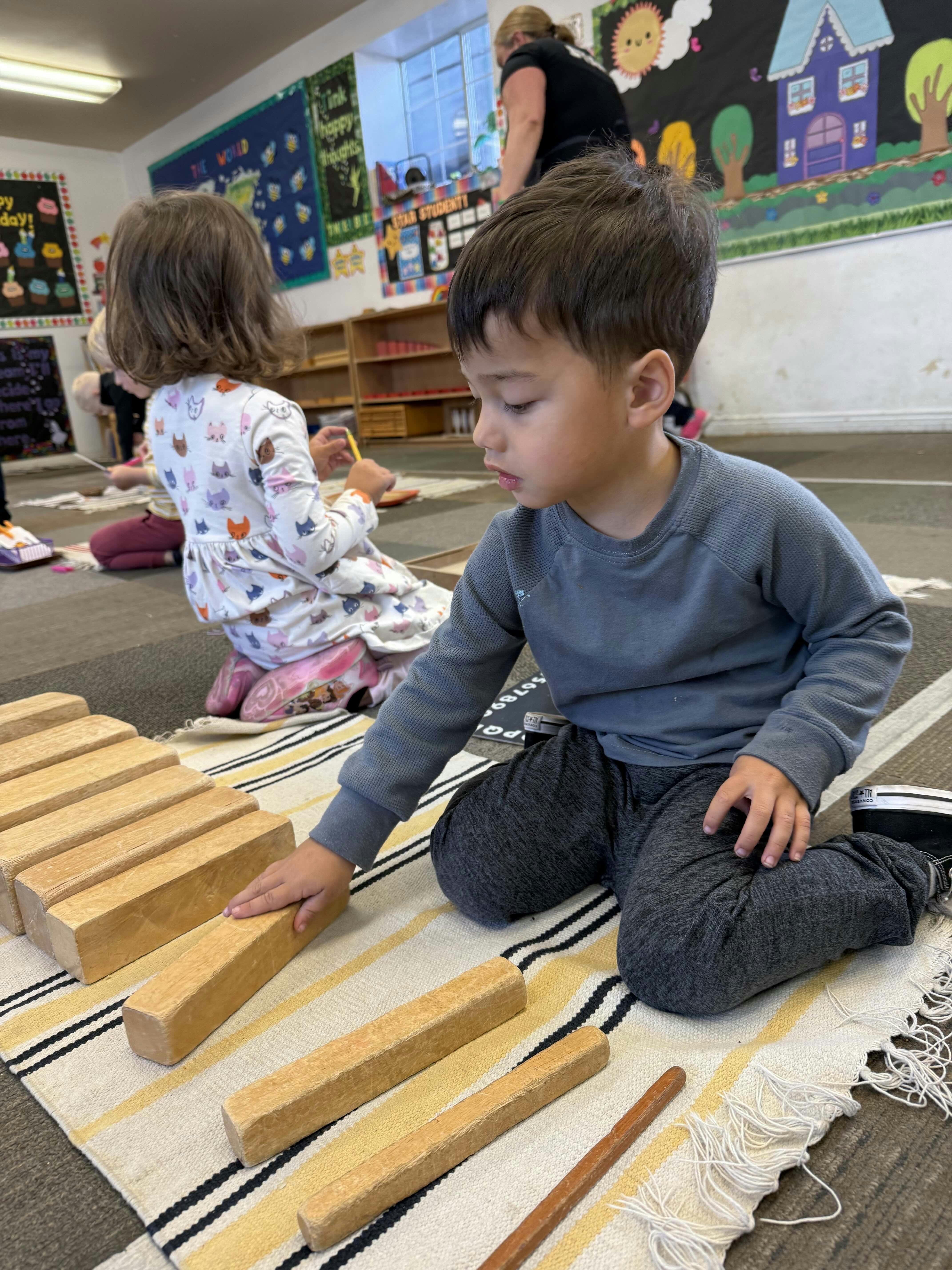 Children sitting on a rug playing with wooden blocks in a classroom