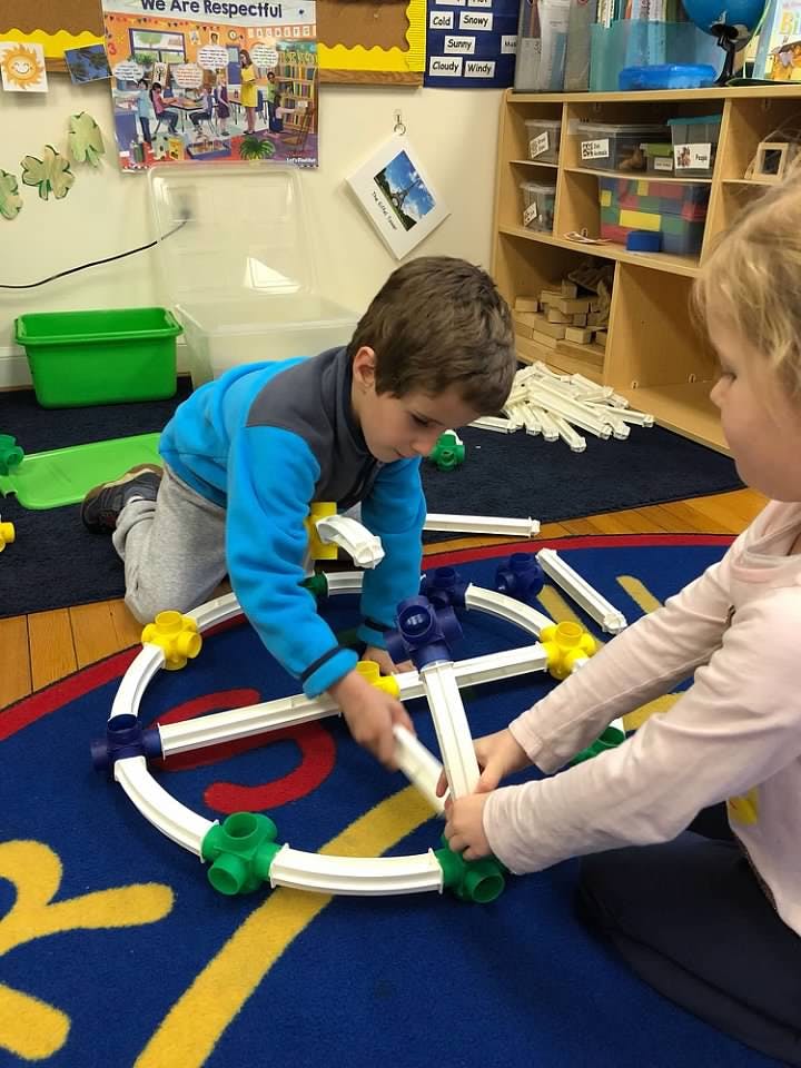 Two children building with construction toys on a classroom floor
