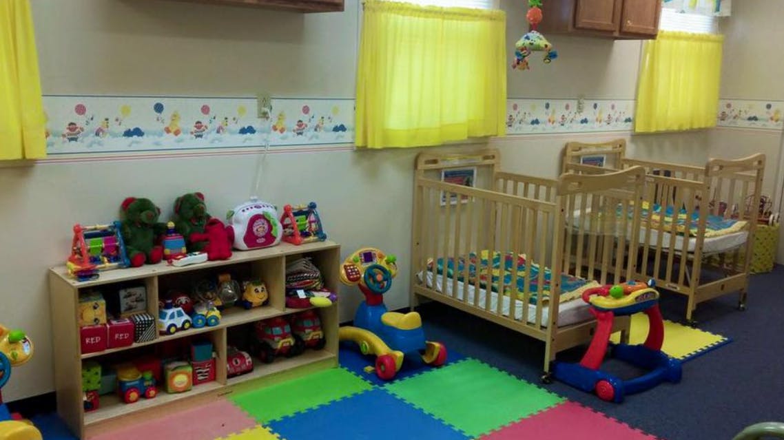 Nursery room with cribs, toy shelf, and play mat