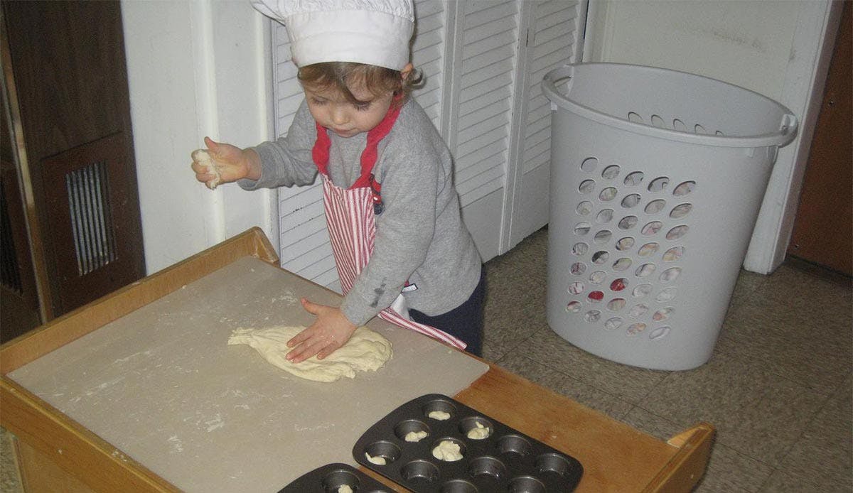 Child in chef hat and apron kneading dough on a table