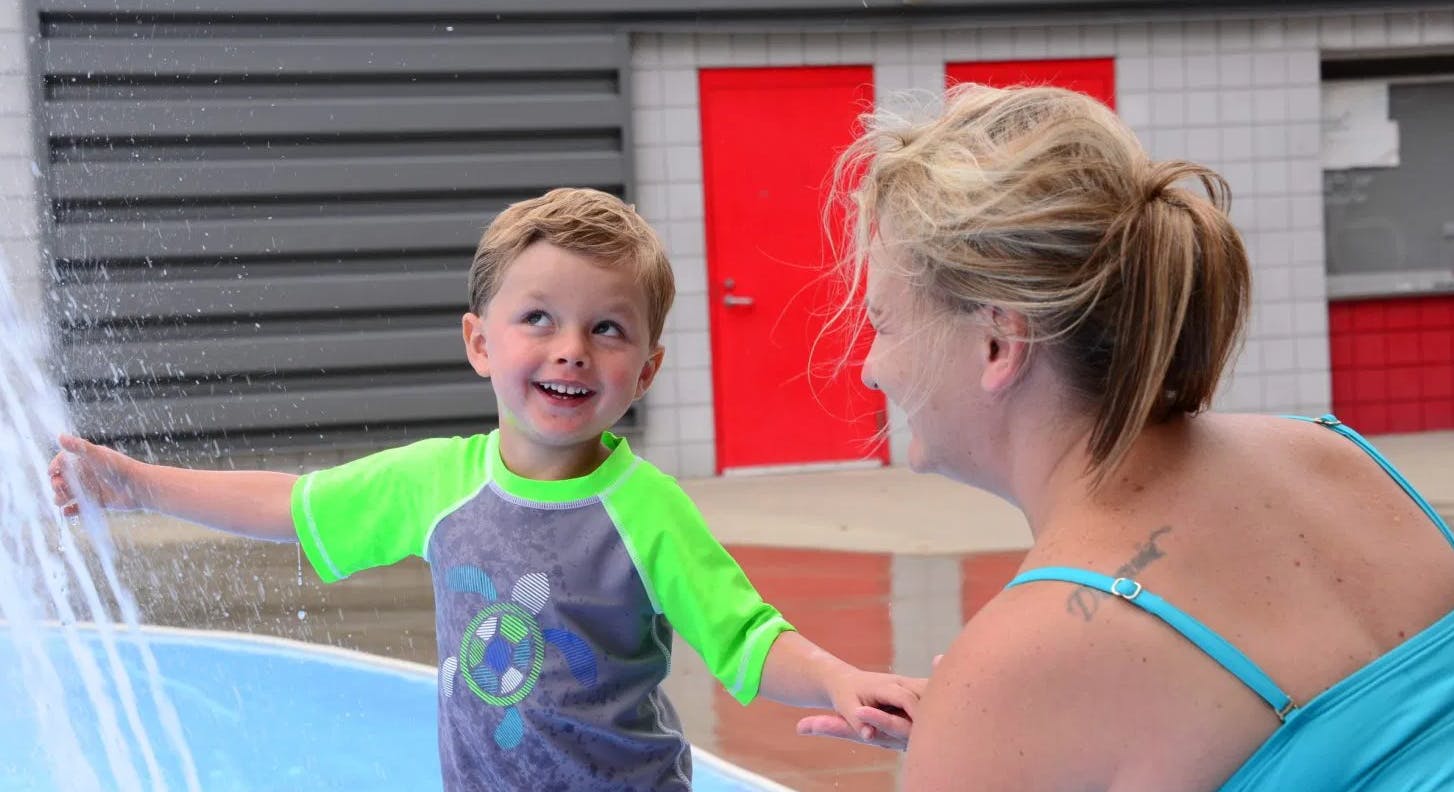 Child playing in water with a person watching