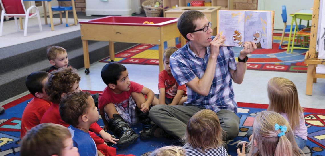 Person reading a book to a group of children in a classroom