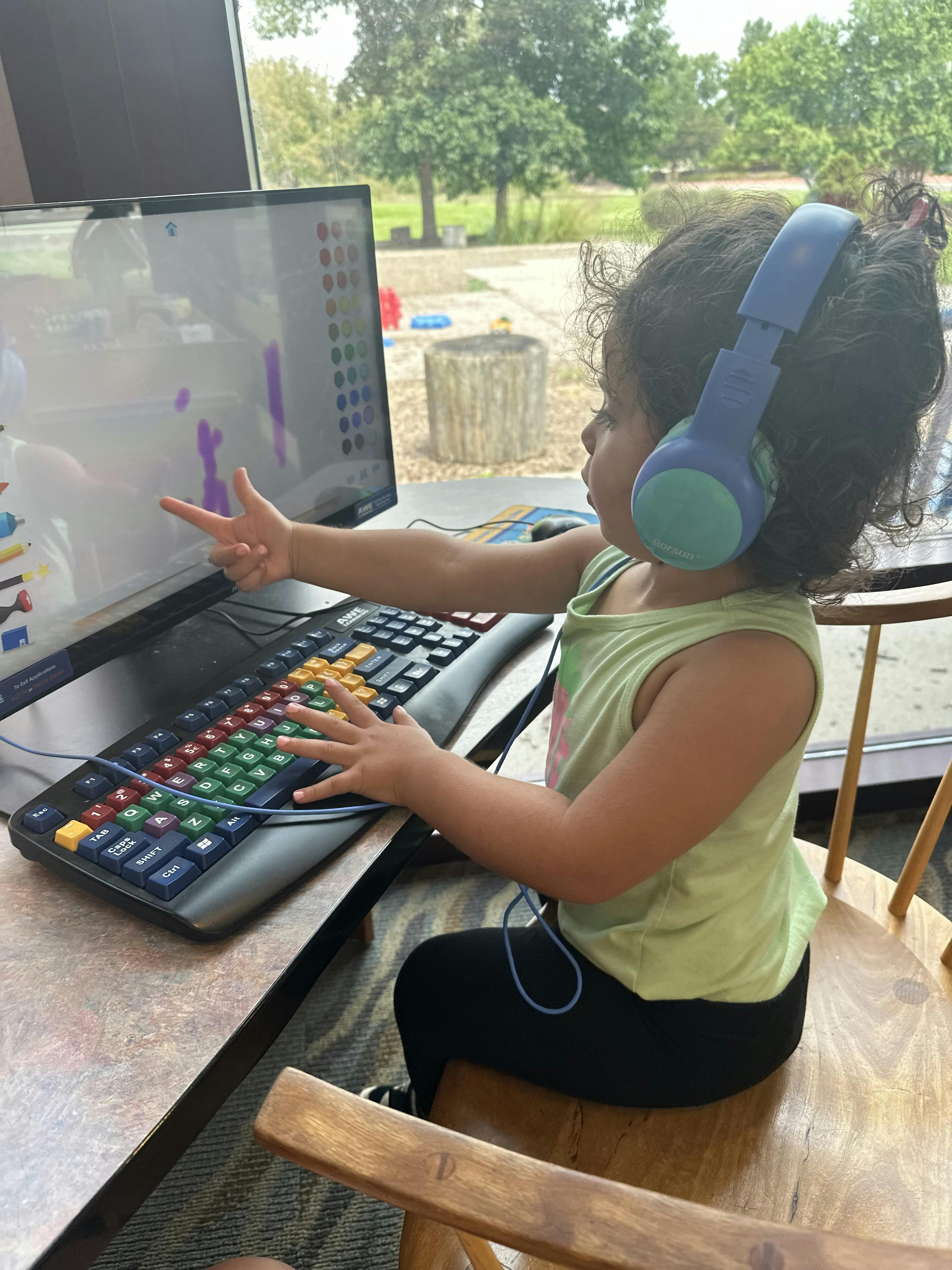Child wearing headphones pointing at a computer screen with a colorful keyboard