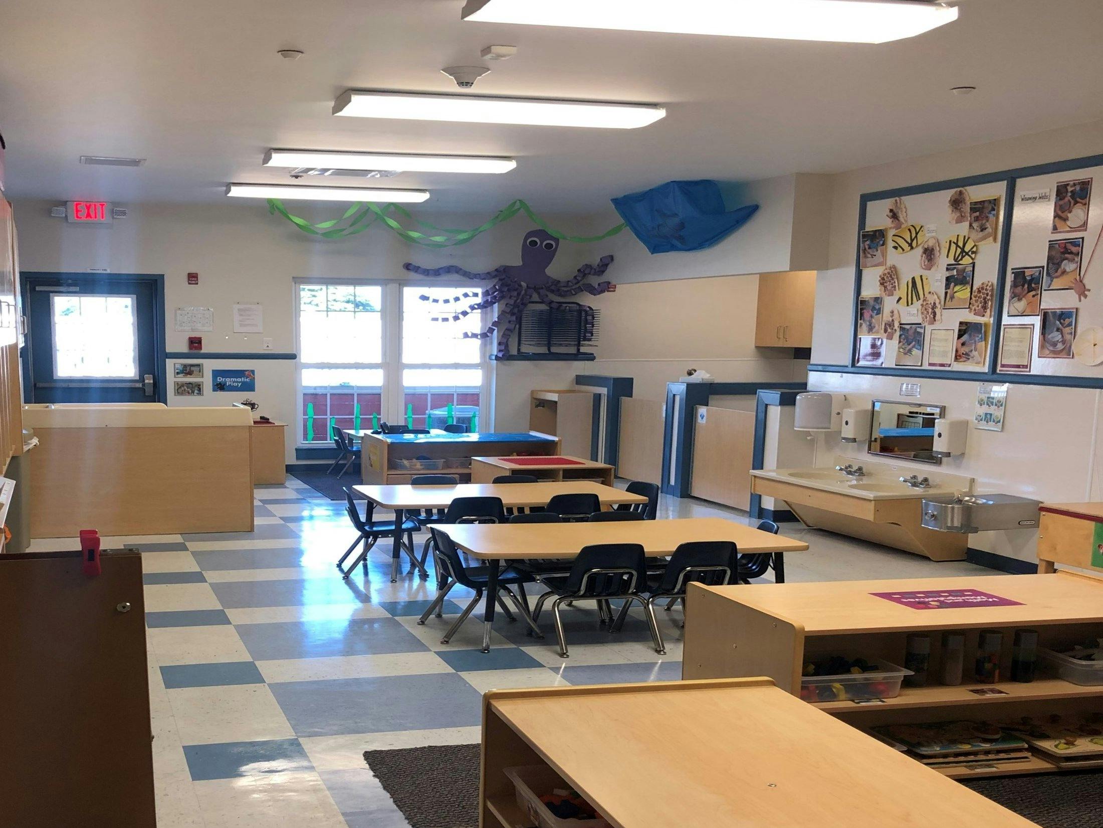 Classroom with small tables and chairs, a sink area, and decorations