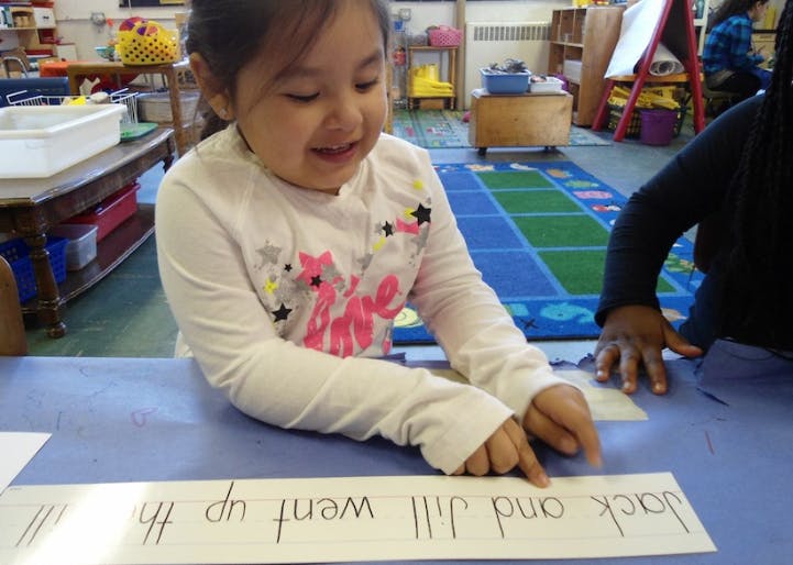 Child pointing to text on a paper strip in a classroom