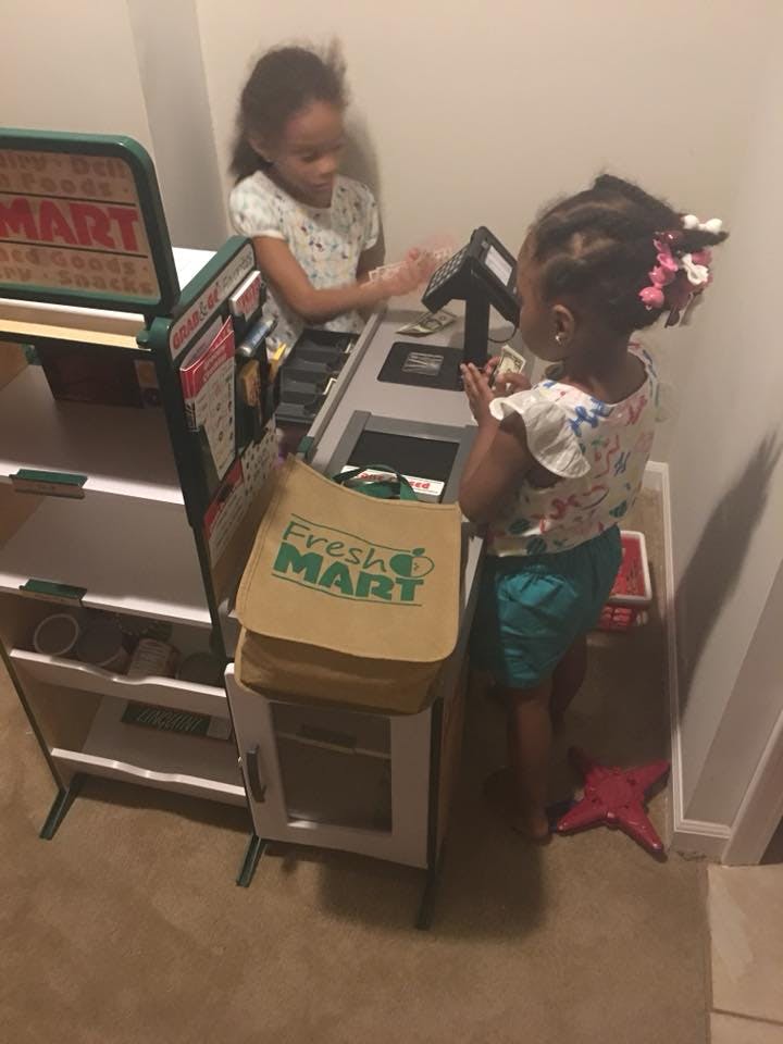 Two children playing at a toy grocery store checkout