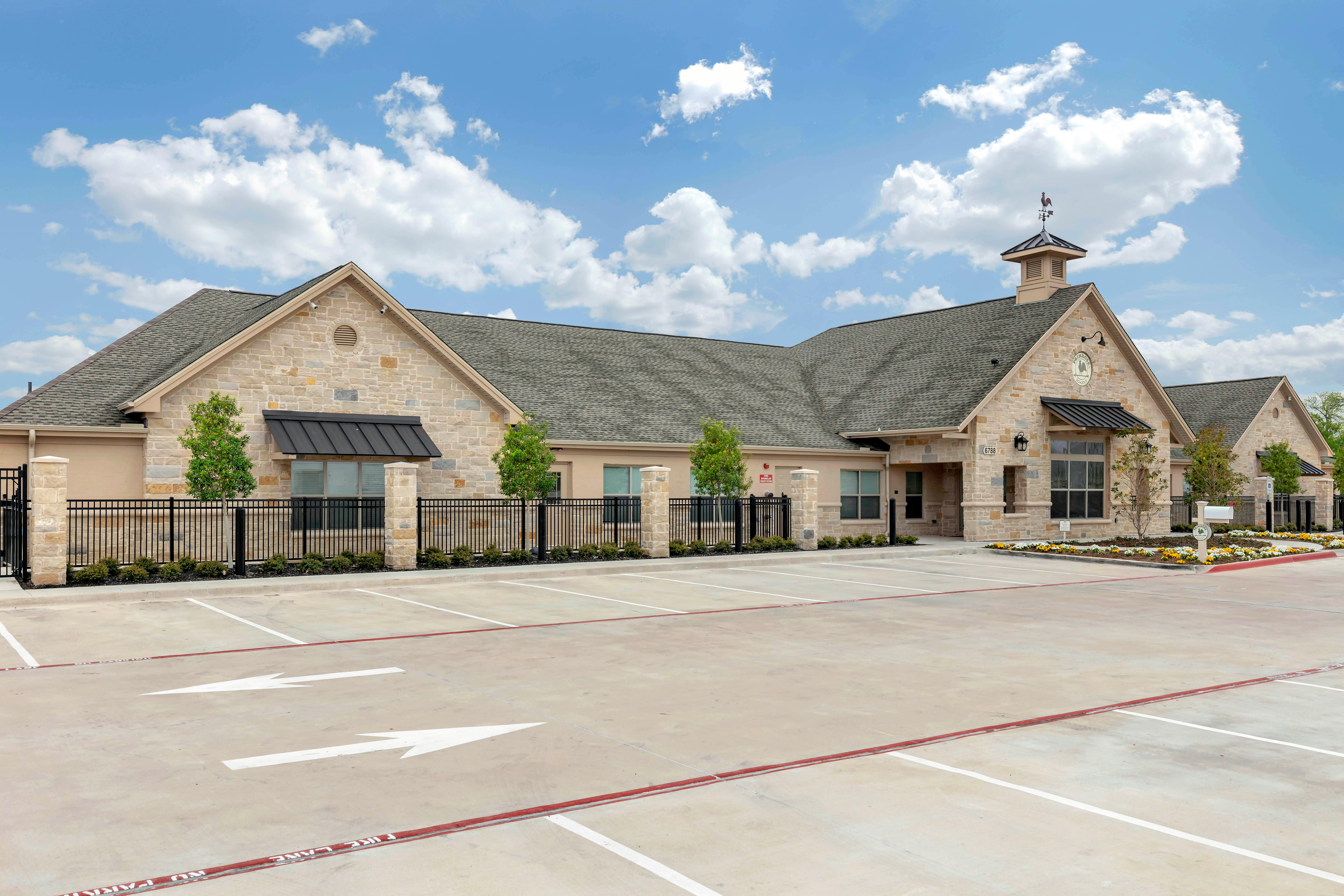 Stone building with a cupola and weather vane, a parking lot in the foreground