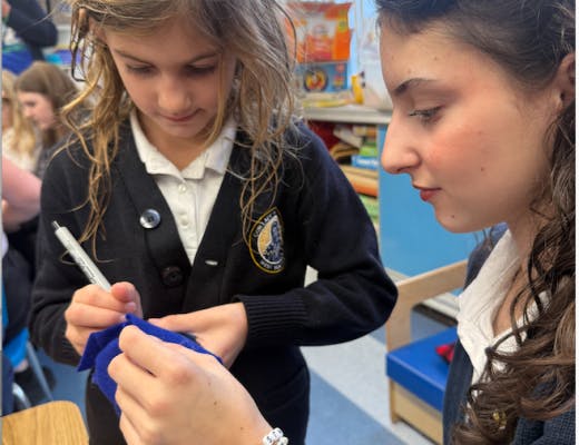 Two girls focused on writing with a pen on a small piece of blue fabric