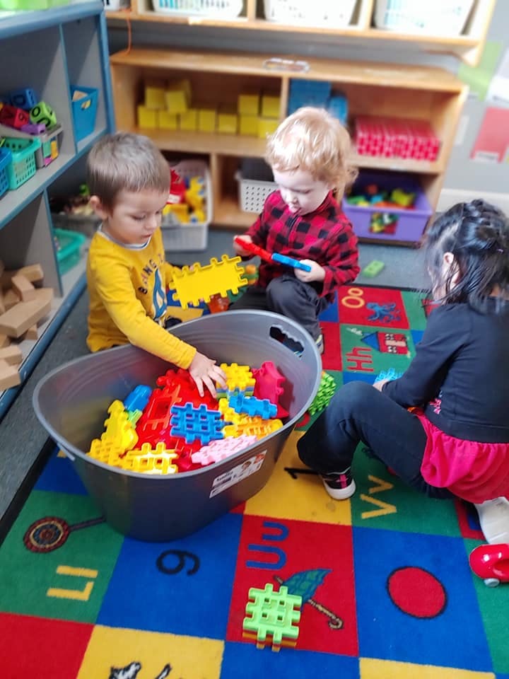 Three children playing with colorful interlocking toys in a classroom