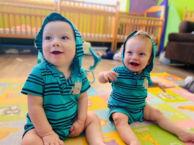 Two children in matching hooded outfits sitting on a colorful mat