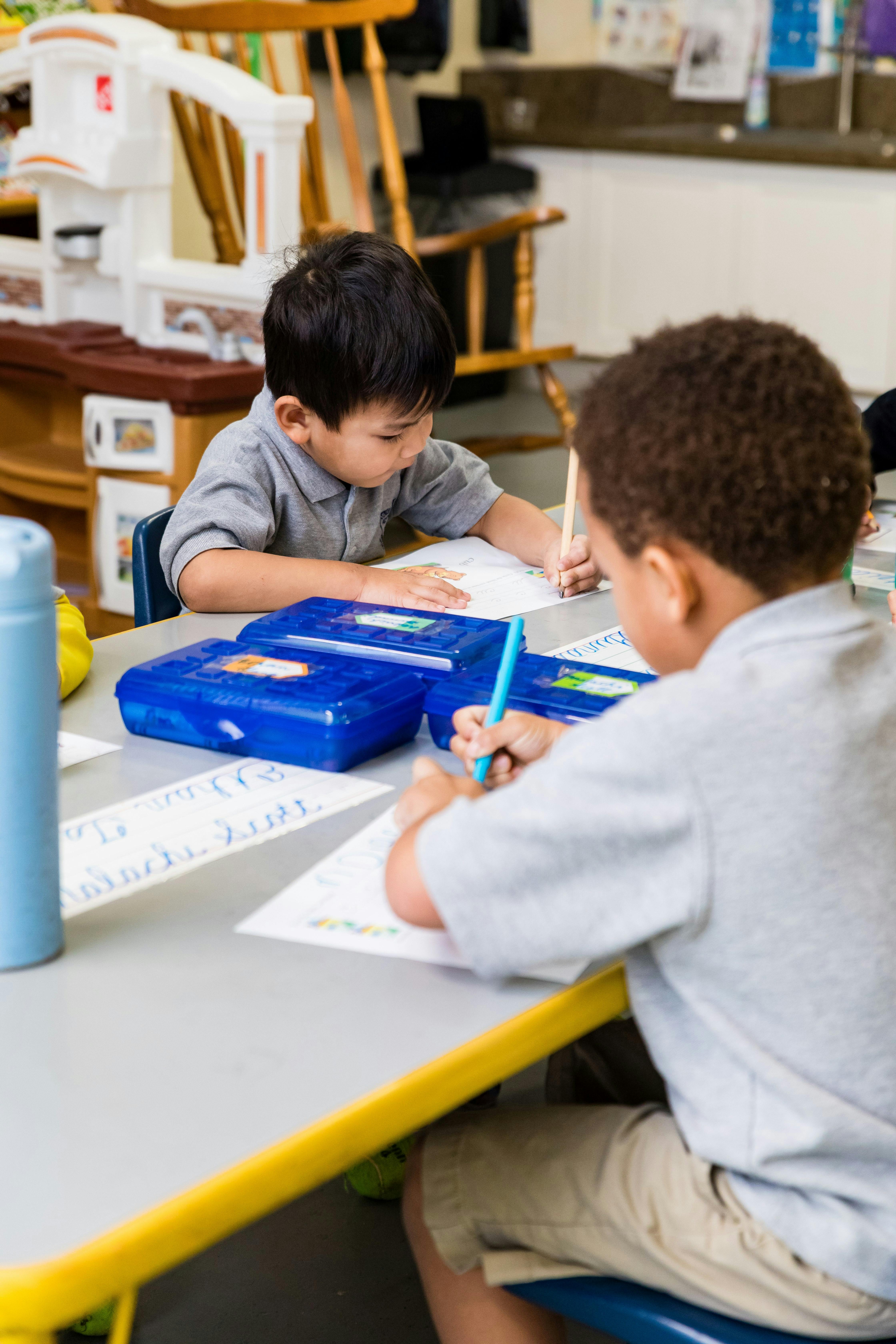 Two children writing at a table in a classroom