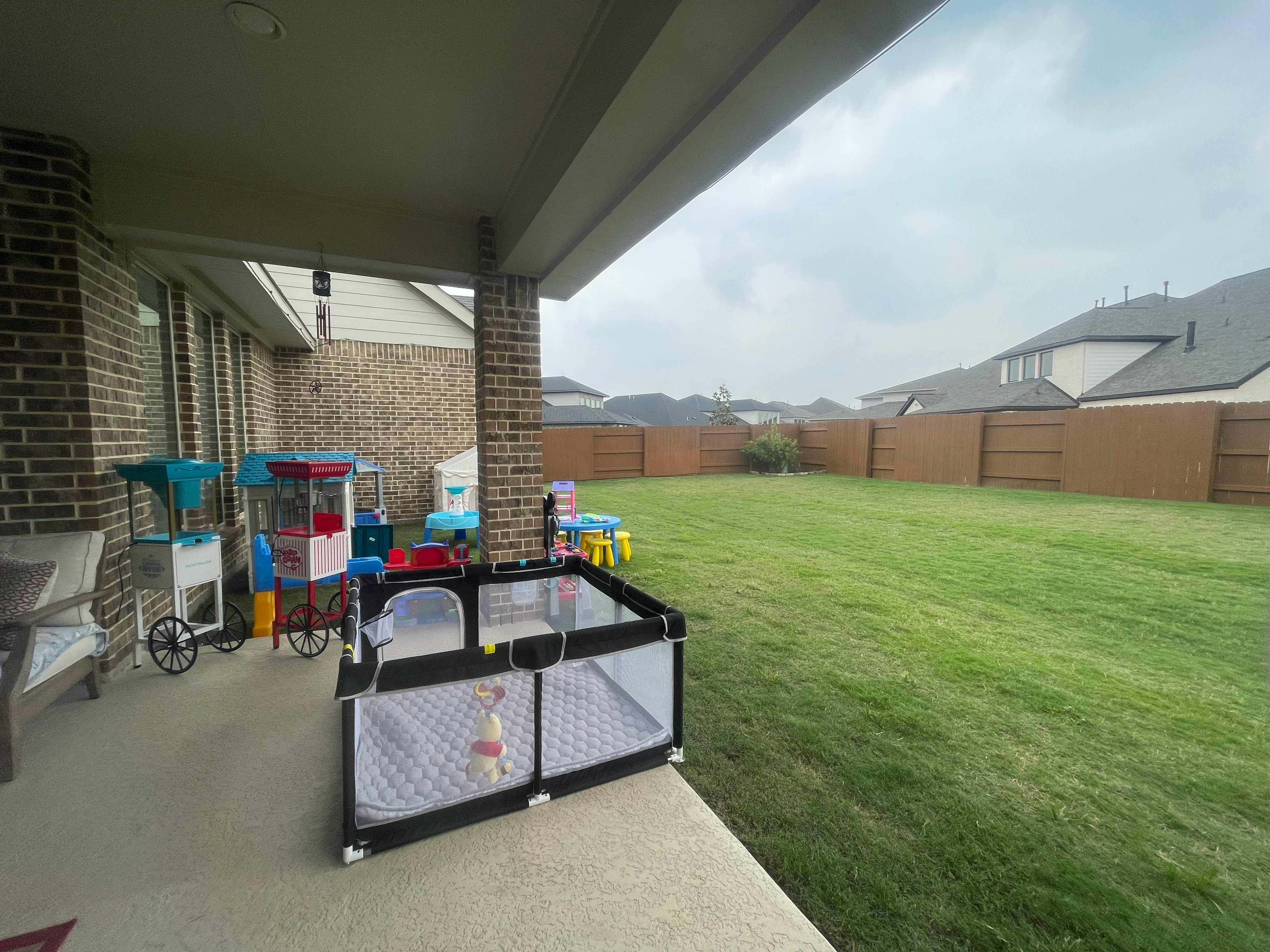 Patio with playpen and toys next to a grassy backyard