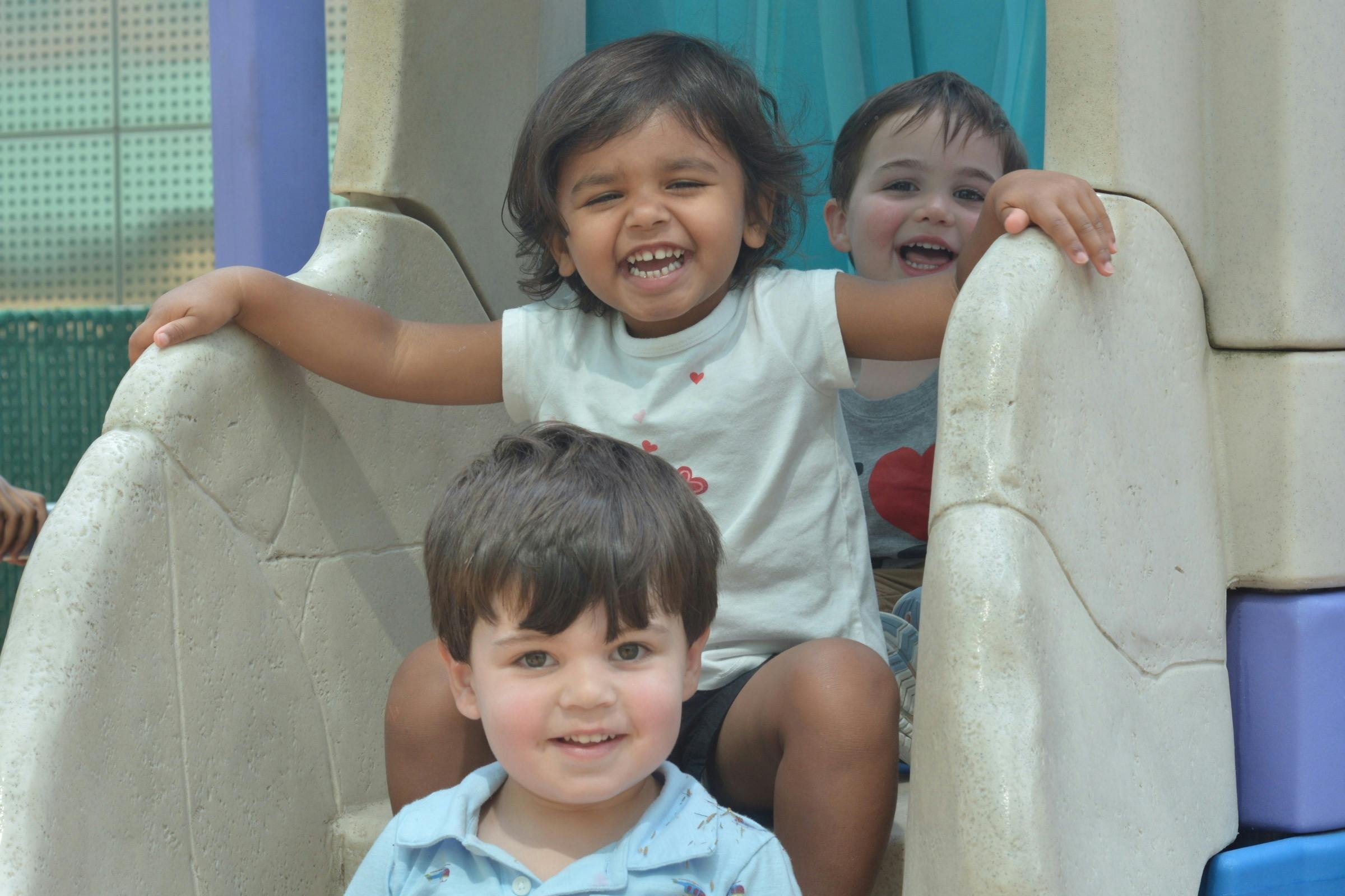 Three children smiling and sitting on a playground slide