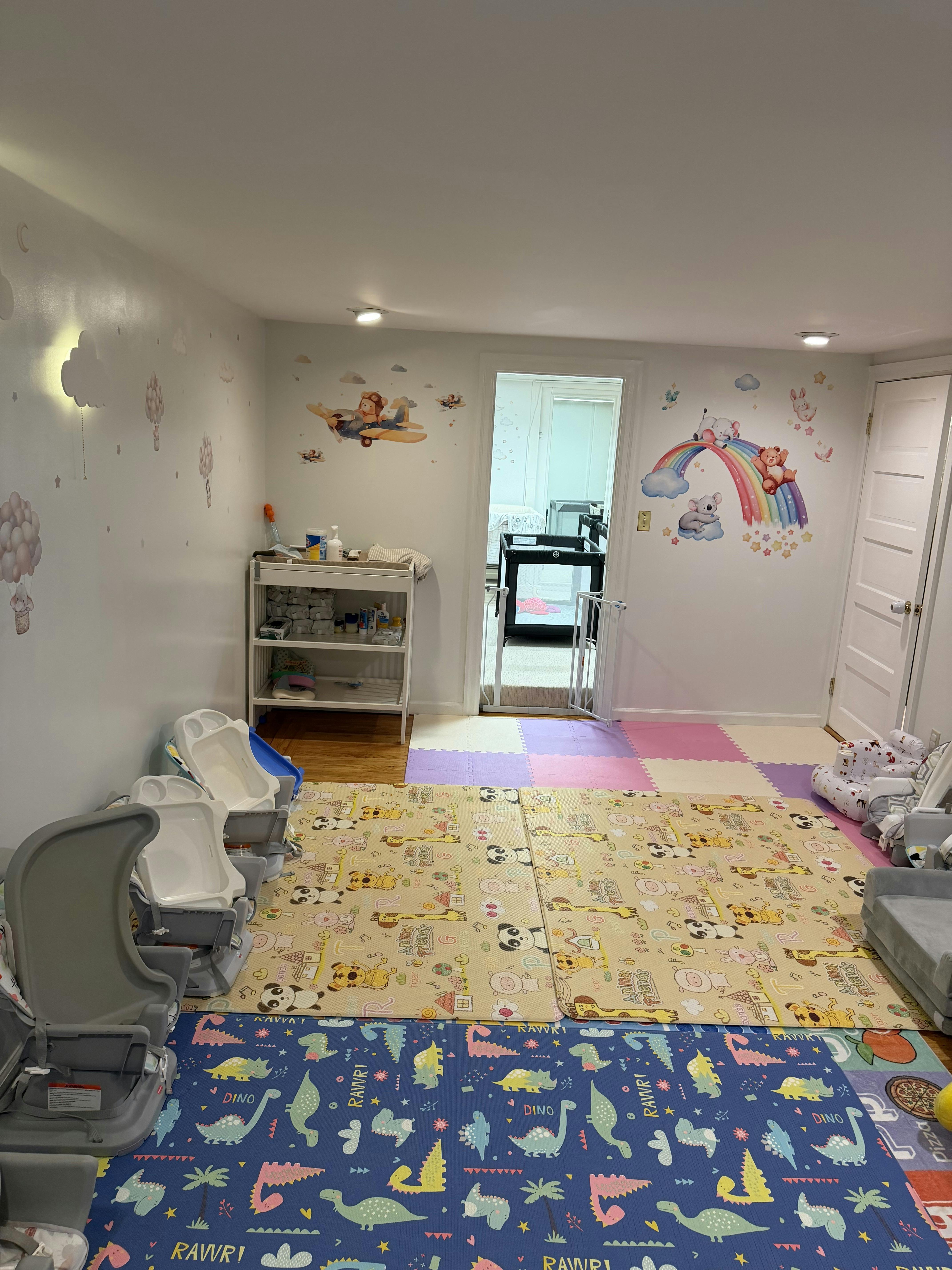 Childcare room with colorful playmats, feeding chairs, and animal wall decals