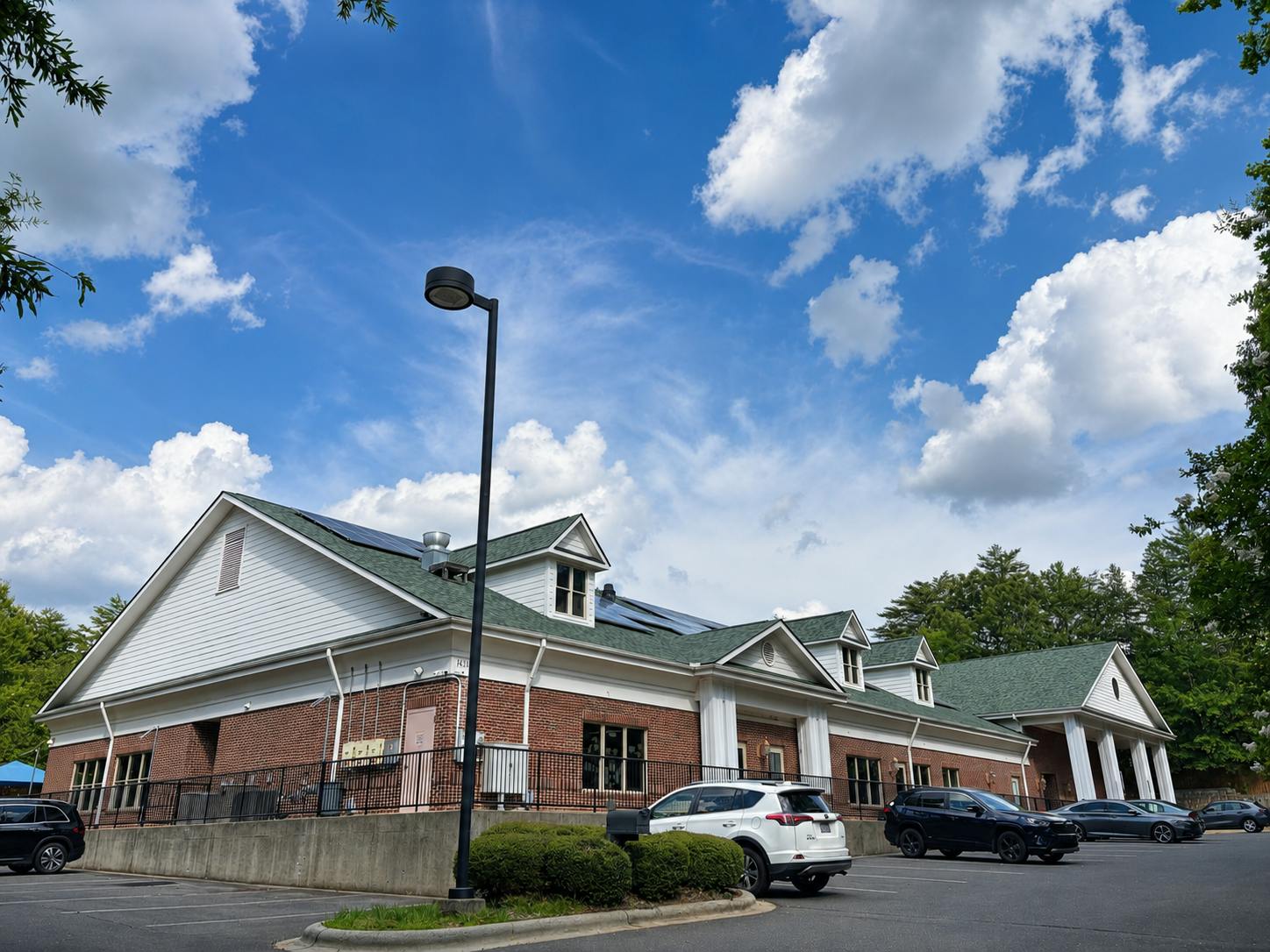 Brick building with white siding and a green roof in a parking lot