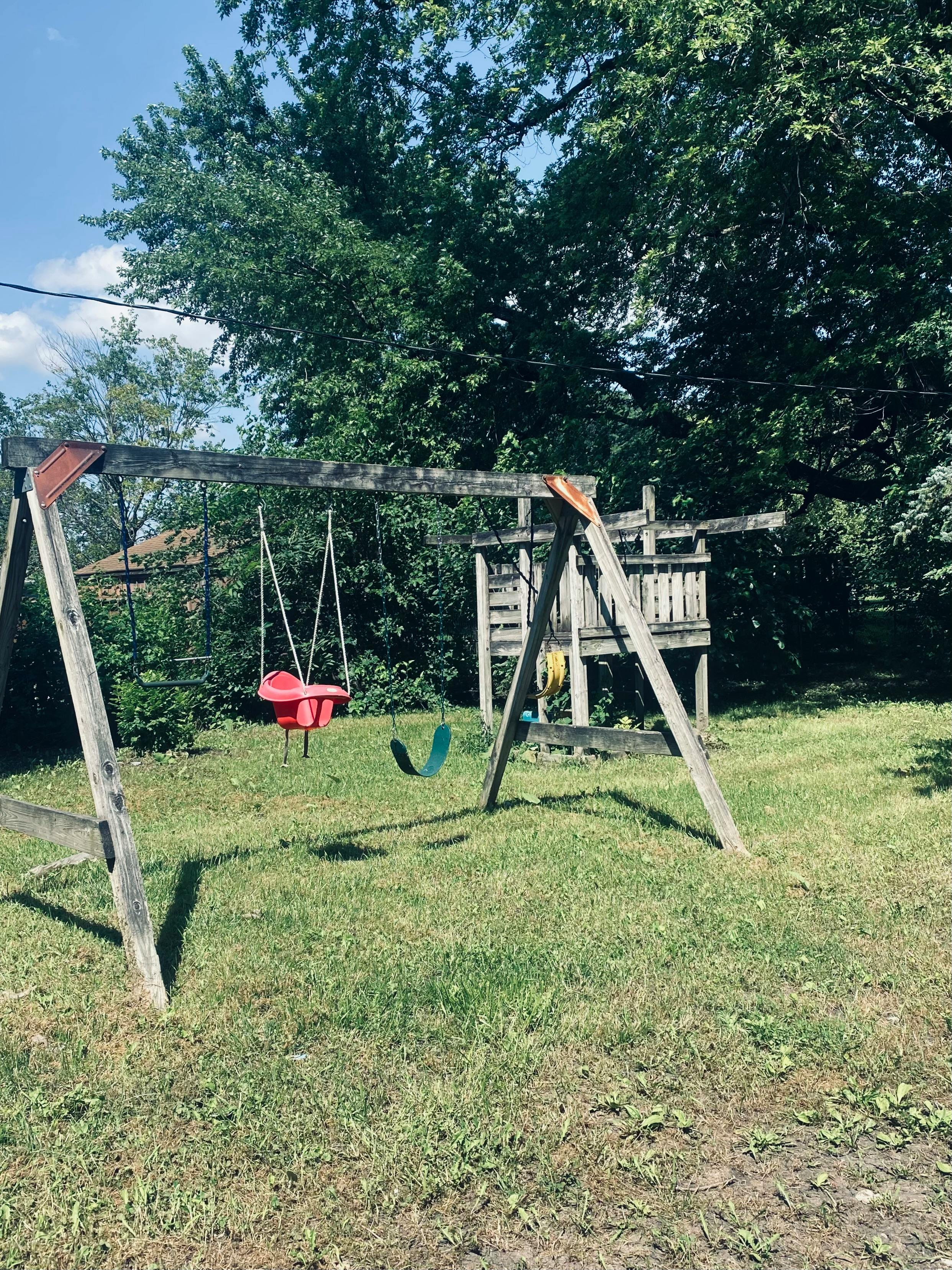 Wooden swing set with red and green swings in a grassy yard