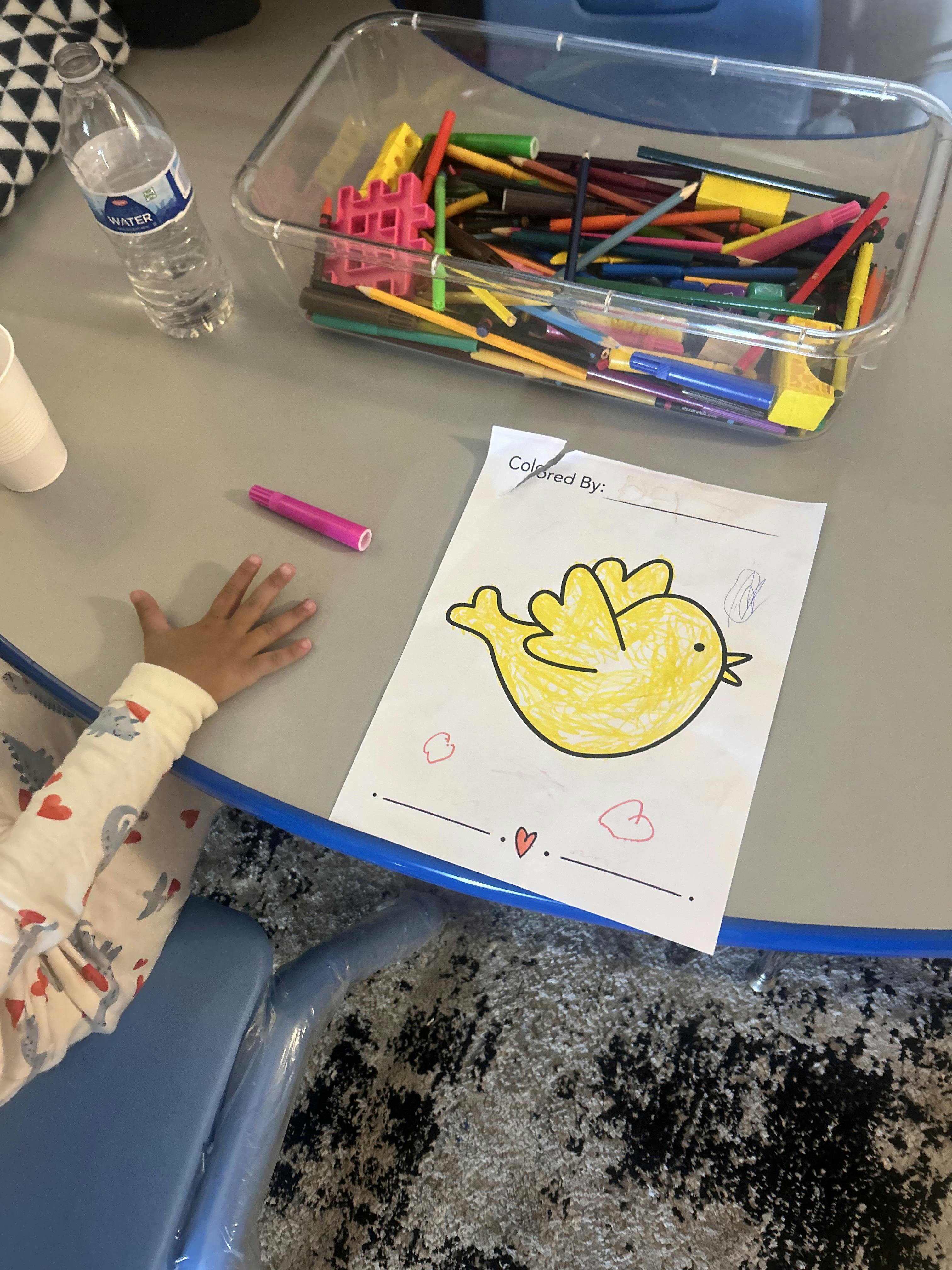 Child reaching for a marker next to a colored drawing of a bird