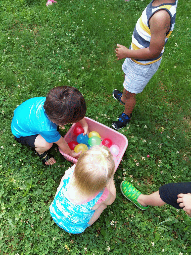Children playing with water balloons in a pink bin on grass